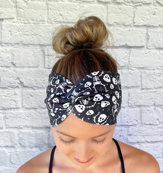 Woman with hair in bun wearing wide, twisted, black headband with white skeleton print.