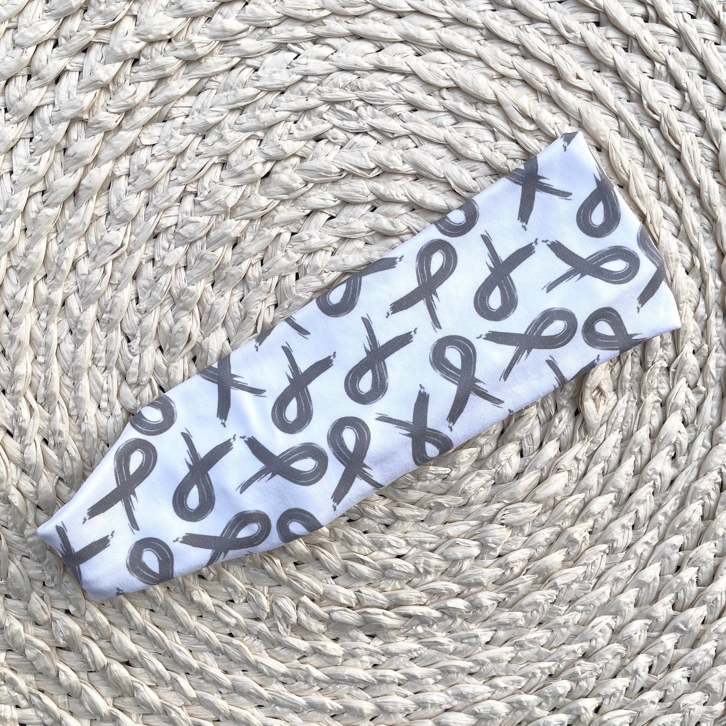 white, flat, stretchy headband with gray ribbon print displayed on a cream background