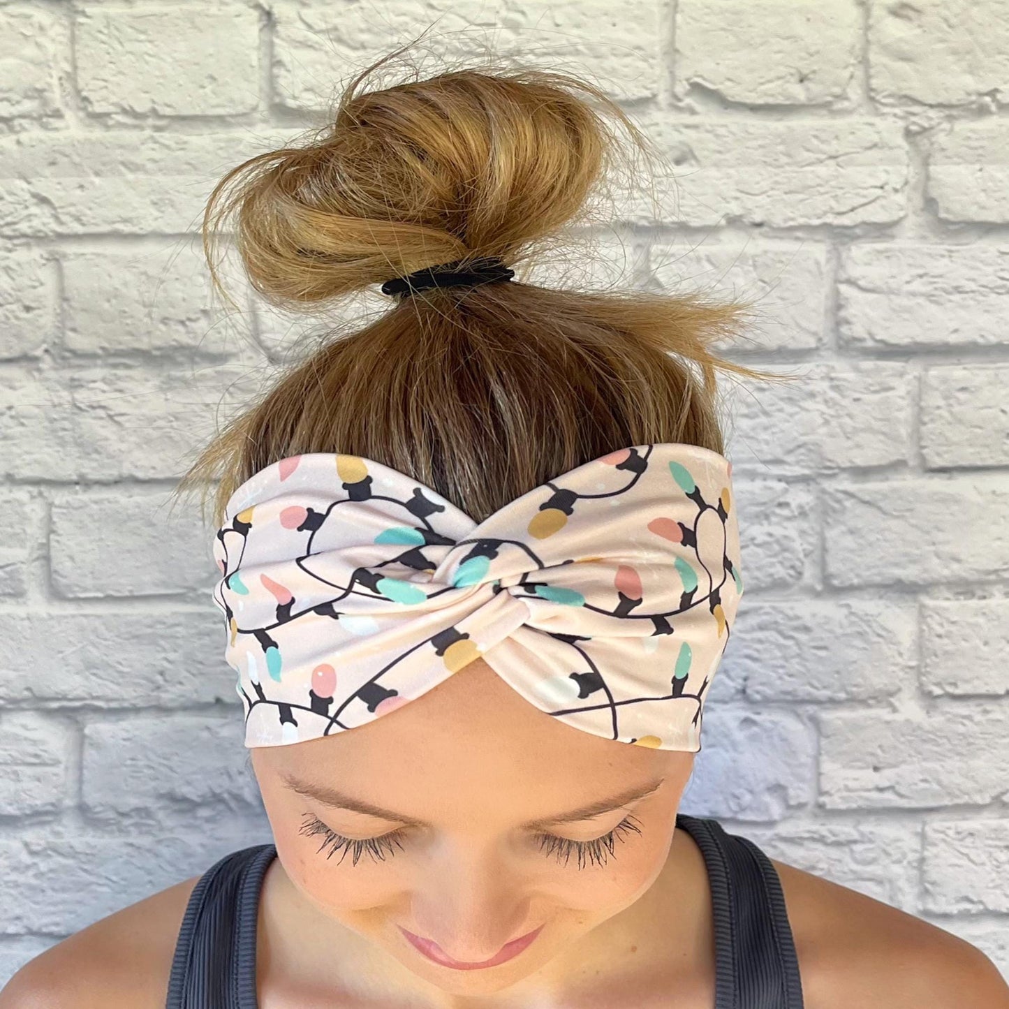 Woman with hair in bun wearing wide, twisted, pink headband with Christmas light print.