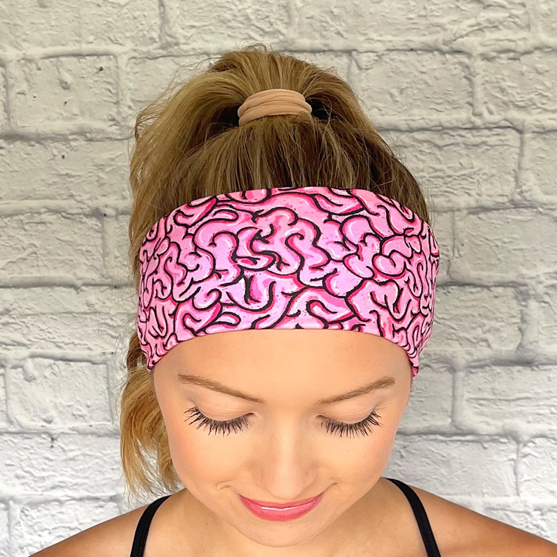Woman with hair in ponytail wearing pink headband with pink/black brain print.