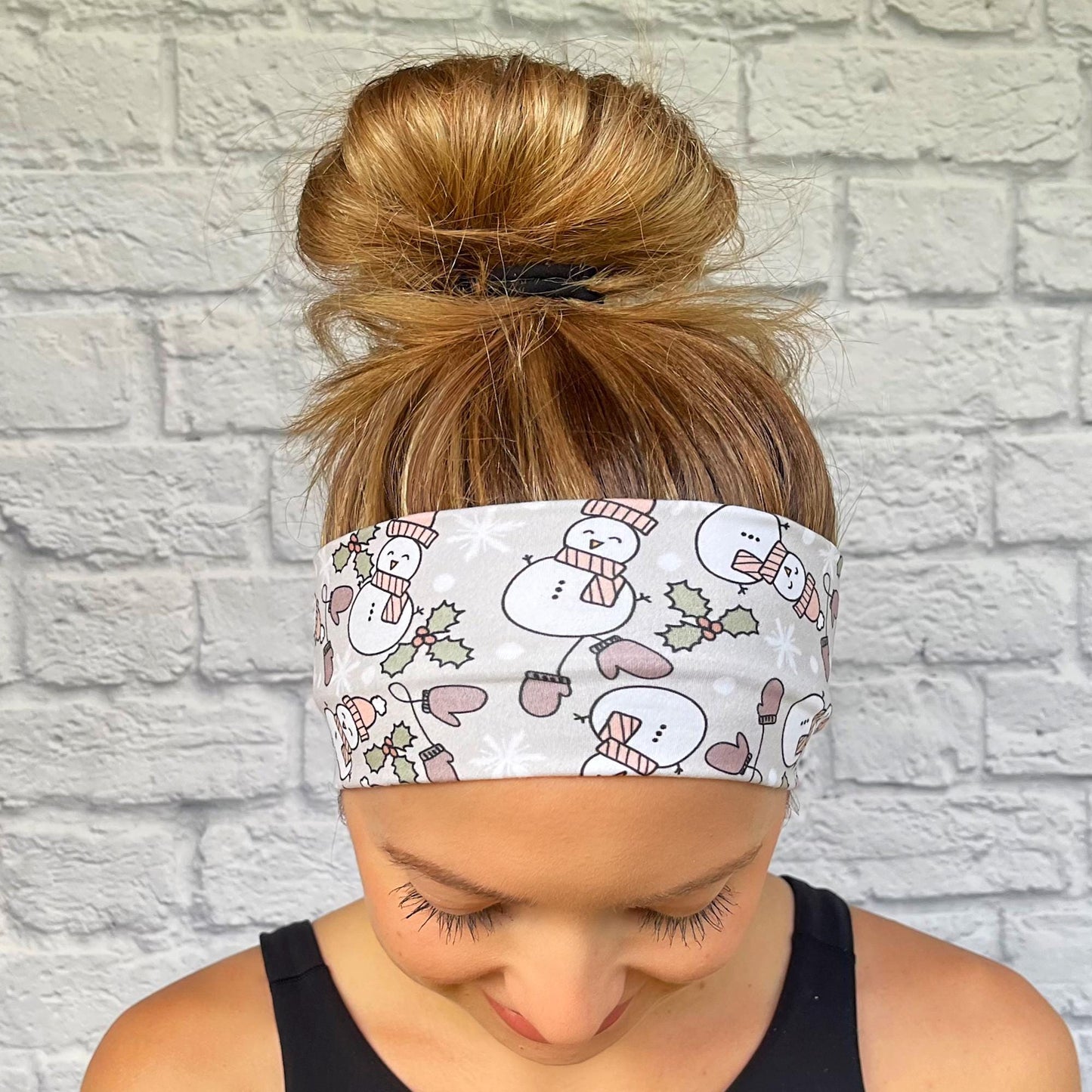 Woman with hair in bun wearing gray, stretchy headband with snowman print, mittens, and Christmas florals.