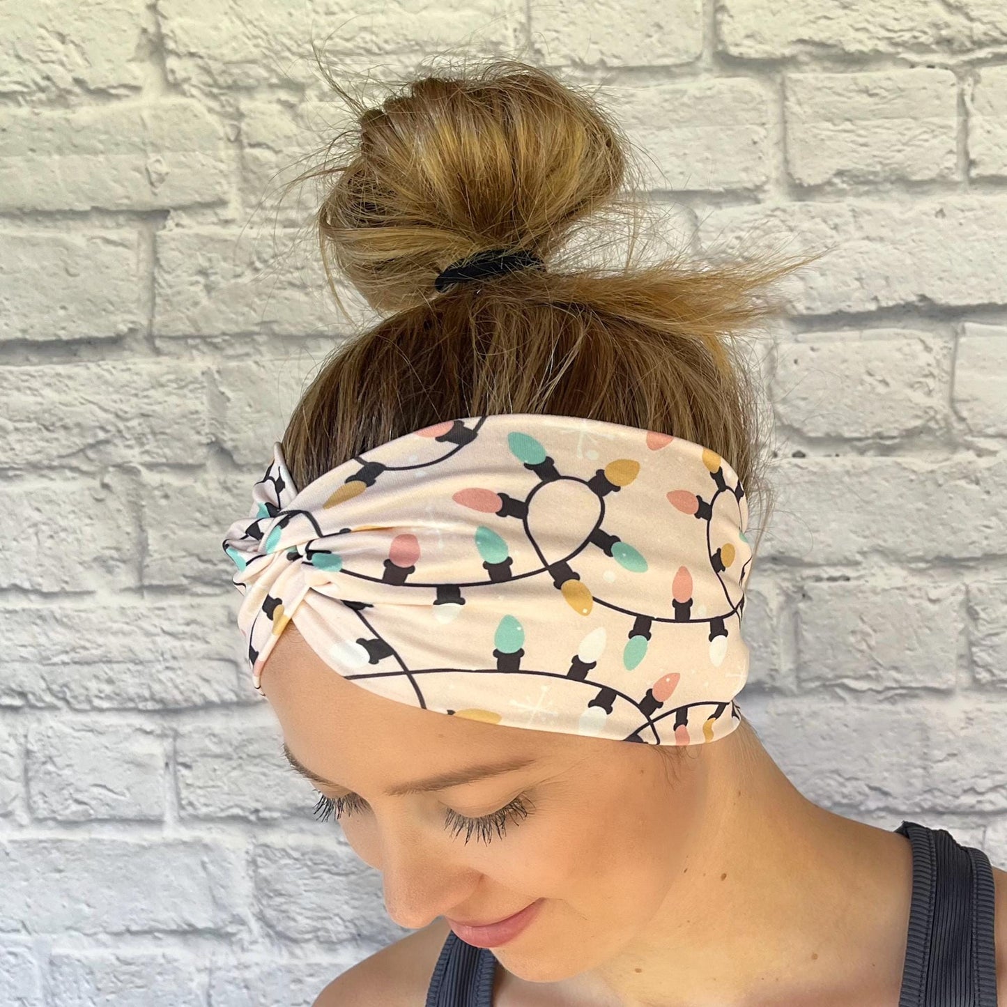 Woman with hair in bun wearing wide, twisted, pink headband with Christmas light print.