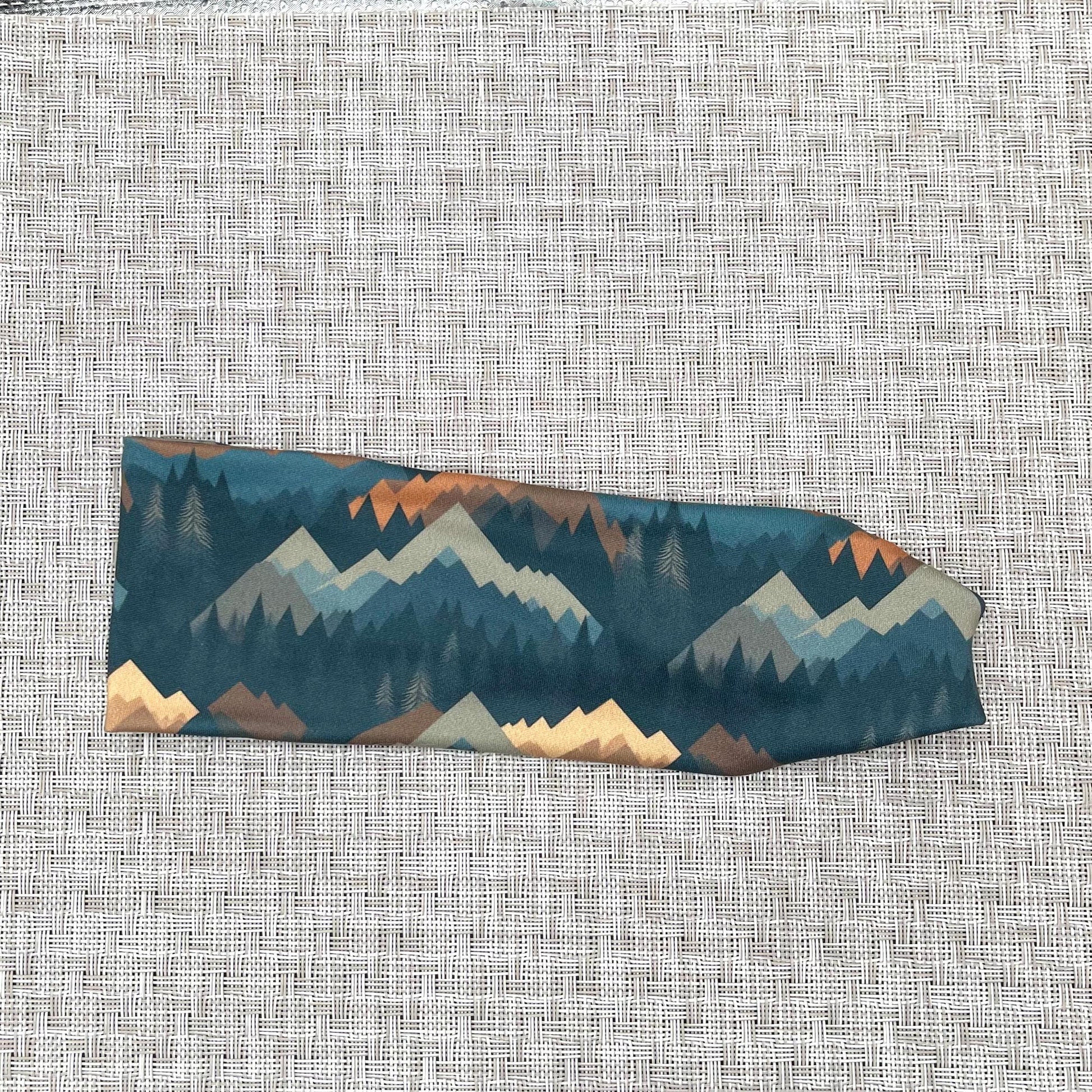 Flat, stretchy headband with mountain print in varying shades of blue, brown, and gray.