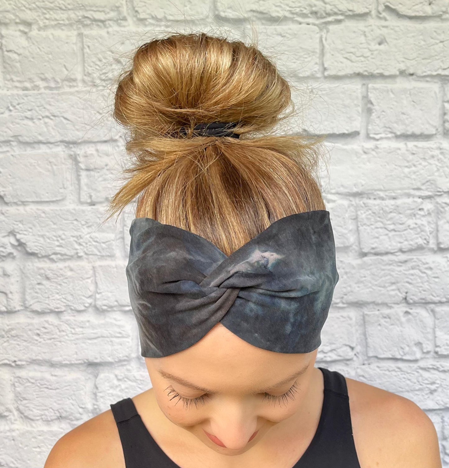 Woman with hair in bun wearing wide, twisted headband in black, gray, silver tie dye print.