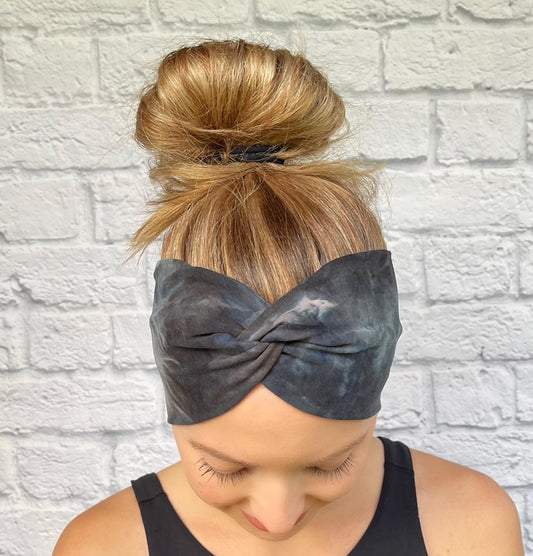 Woman with hair in bun wearing wide, twisted headband in black, gray, silver tie dye print.