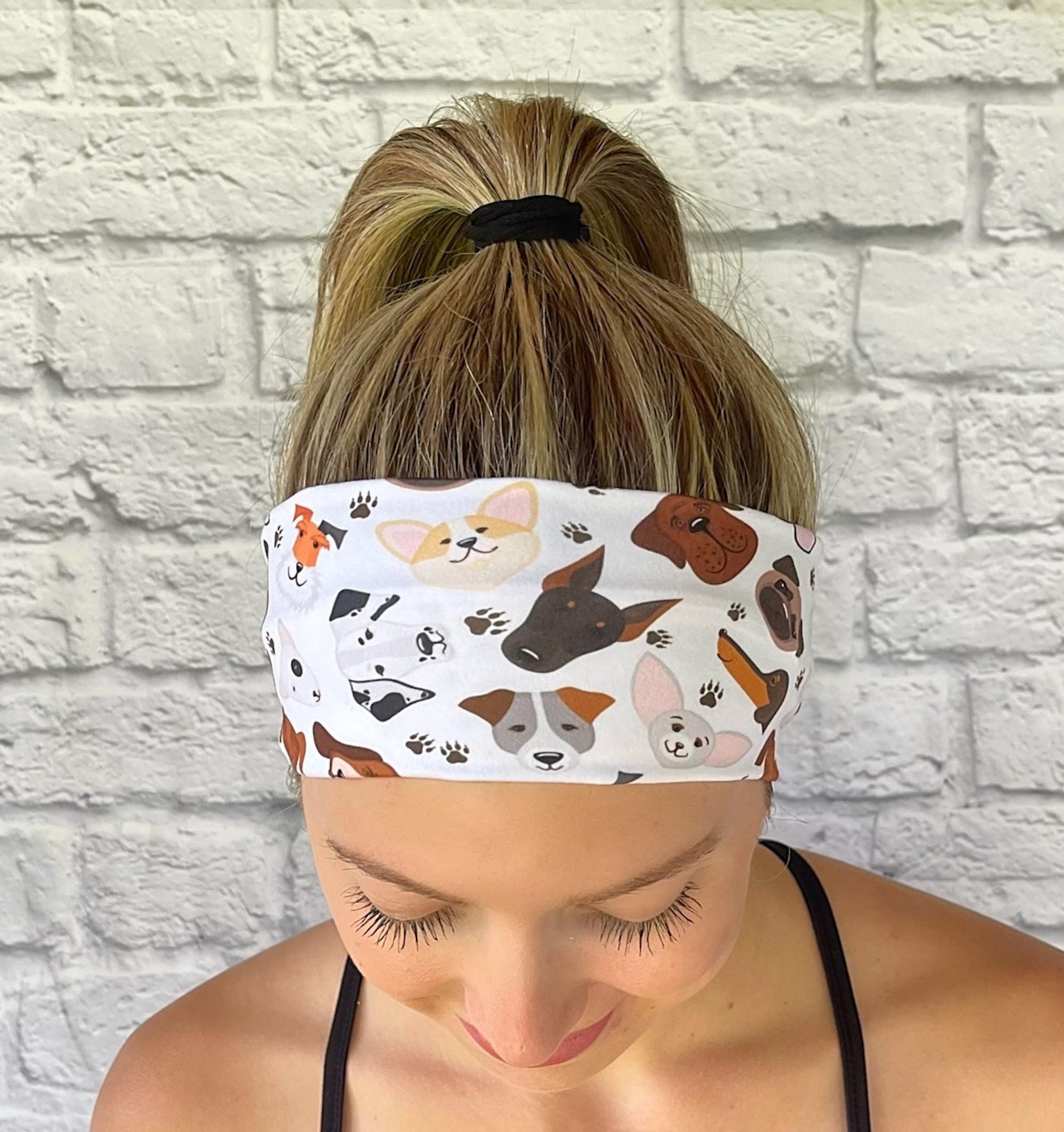 Woman with hair in ponytail wearing flat, stretchy headband in white with dog faces print.