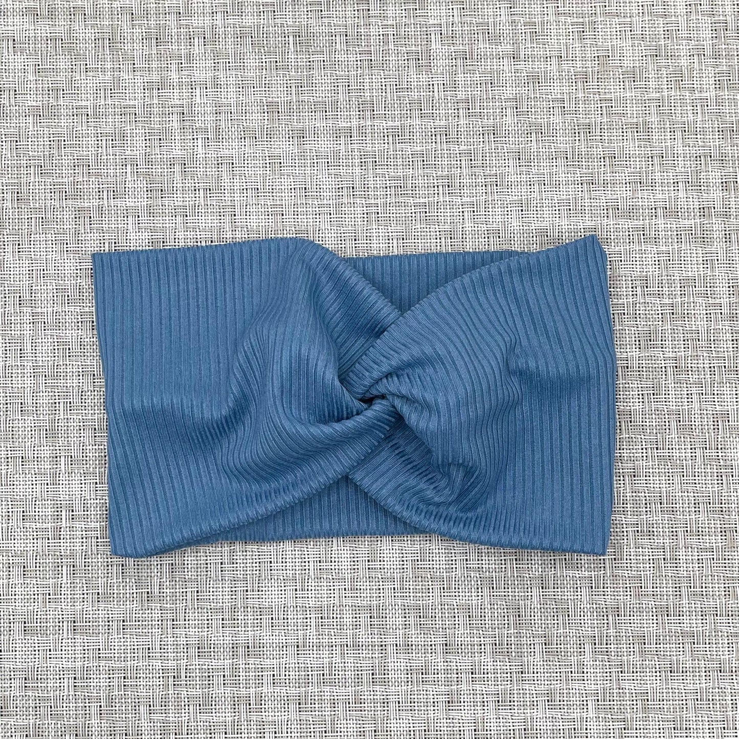 Wide, twisted, stretchy headband in blue ribbed fabric.