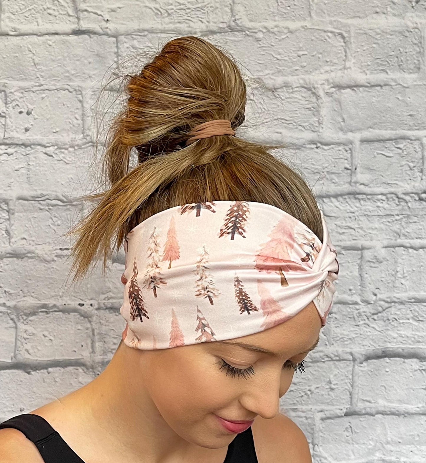 Woman with hair in bun wearing wide, twisted headband in light pink with Christmas tree print.