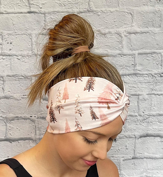 Woman with hair in bun wearing wide, twisted headband in light pink with Christmas tree print.