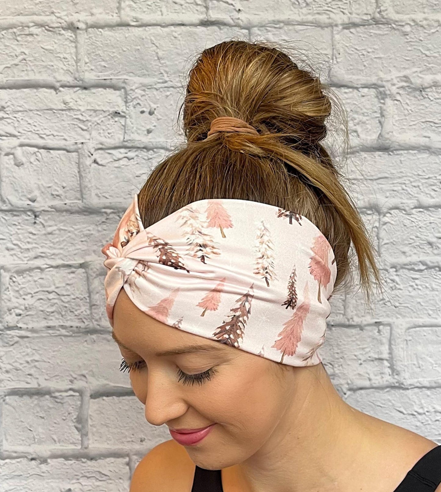 Woman with hair in bun wearing wide, twisted headband in light pink with Christmas tree print.