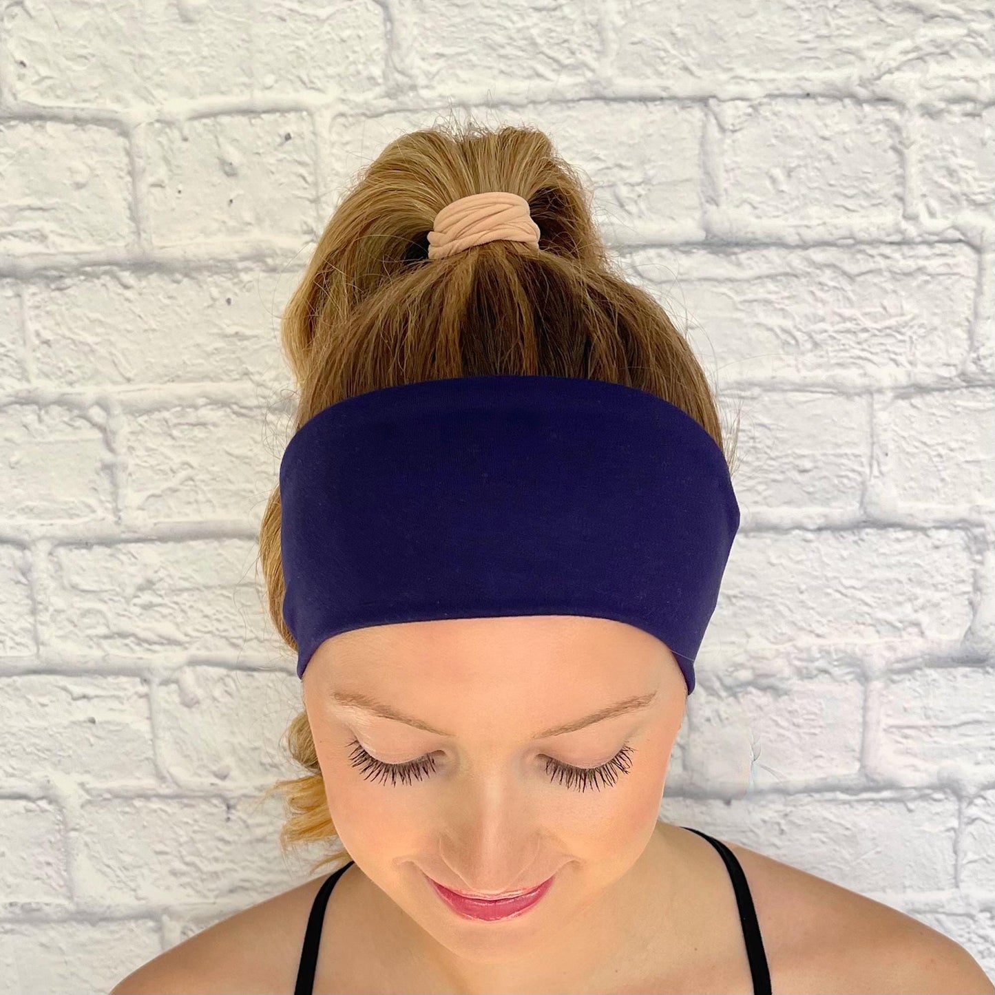 Woman with hair in curled ponytail wearing flat, stretchy headband in dark blue/navy color.