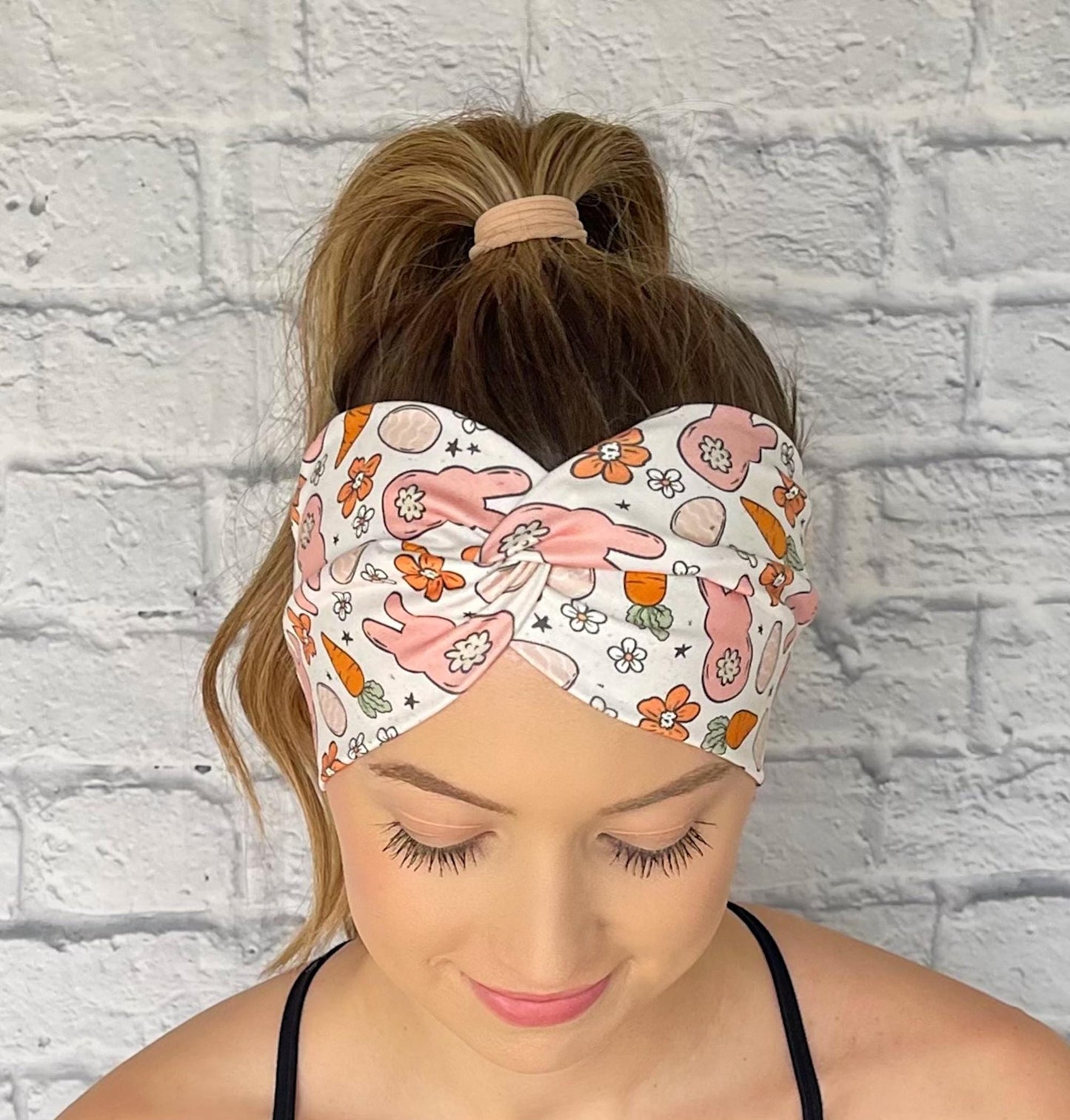Woman with hair in curled ponytail wearing wide, twisted headband in white with orange and peach Easter theme print.