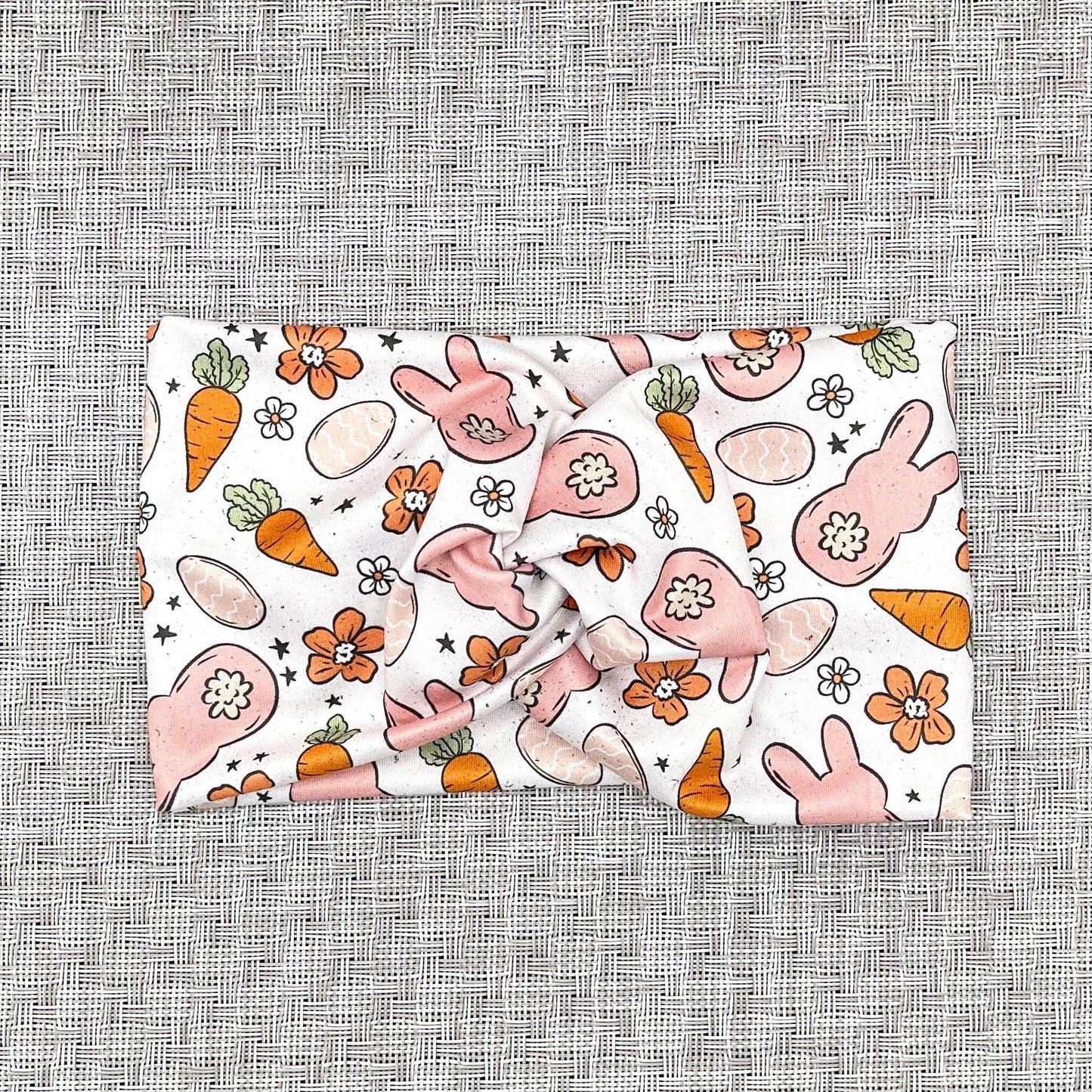Wide, twisted headband in white with orange and peach Easter theme print.