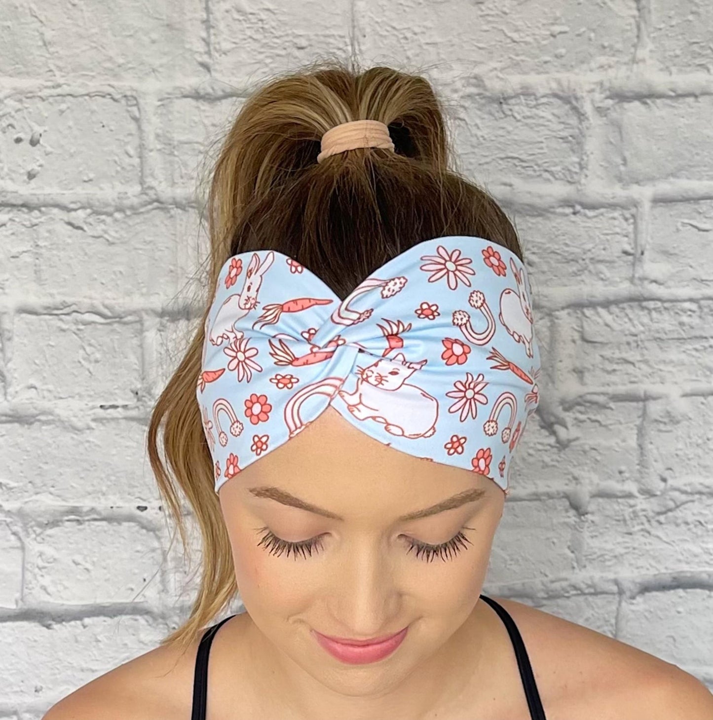 Woman with hair in curled ponytail wearing wide, twisted, light blue headband with Easter theme print.