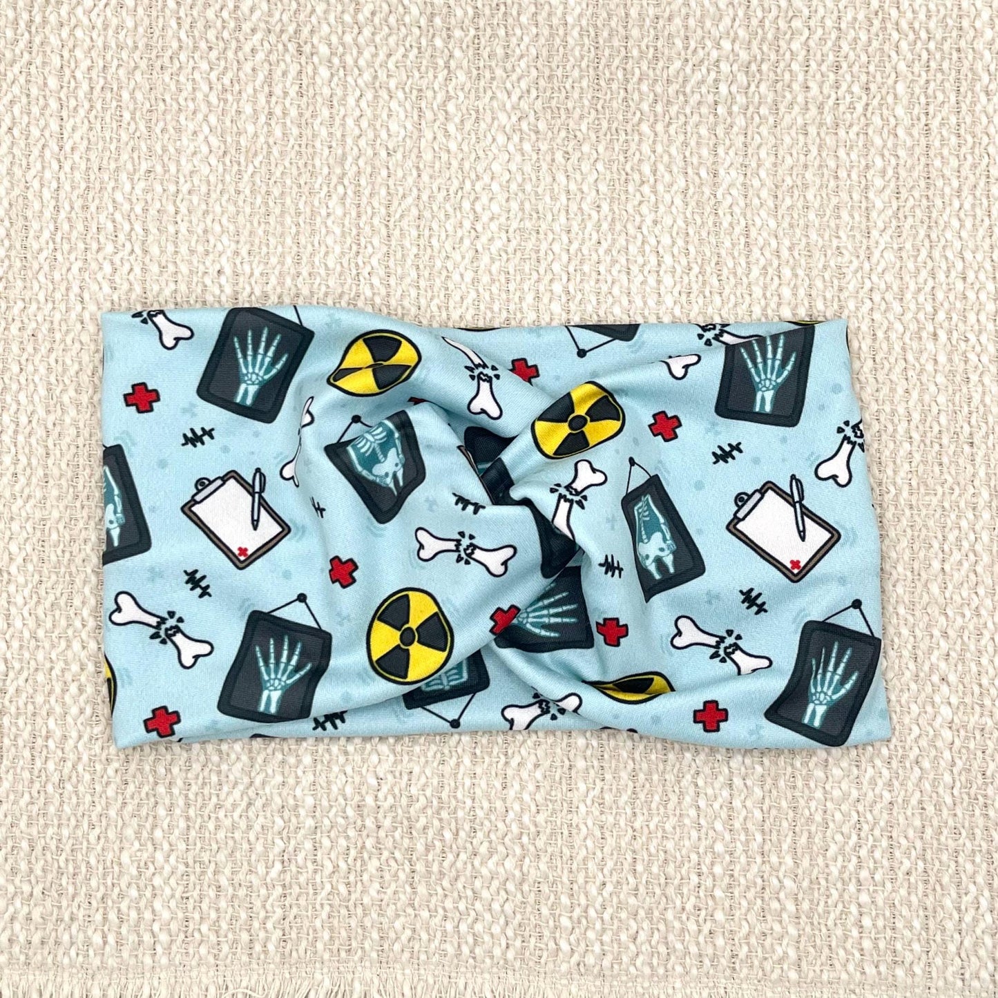 Wide, twisted, blue headband with radiology theme print, displayed on a cream background.