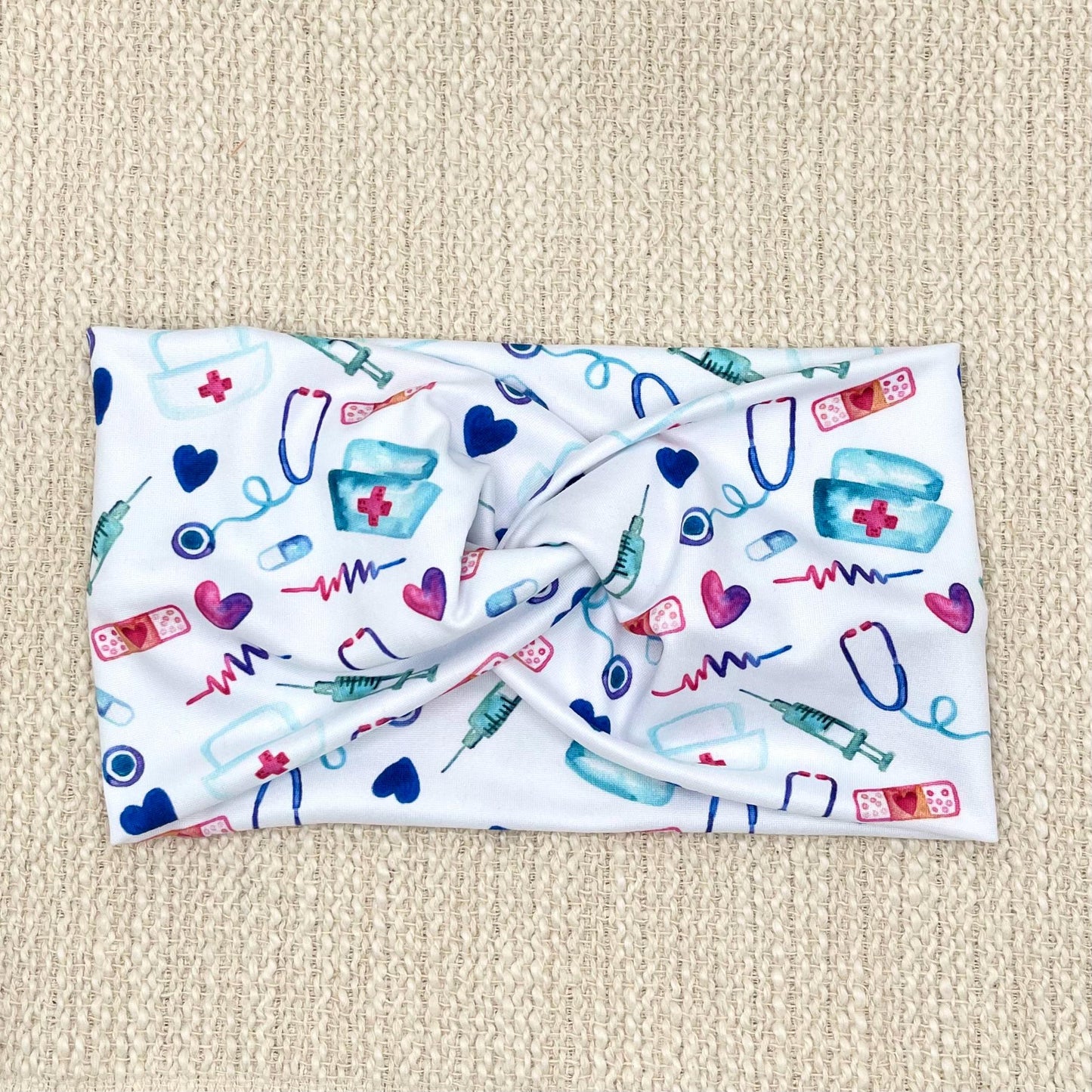 Wide, twisted, white headband with pink, blue, and purple medical theme print.