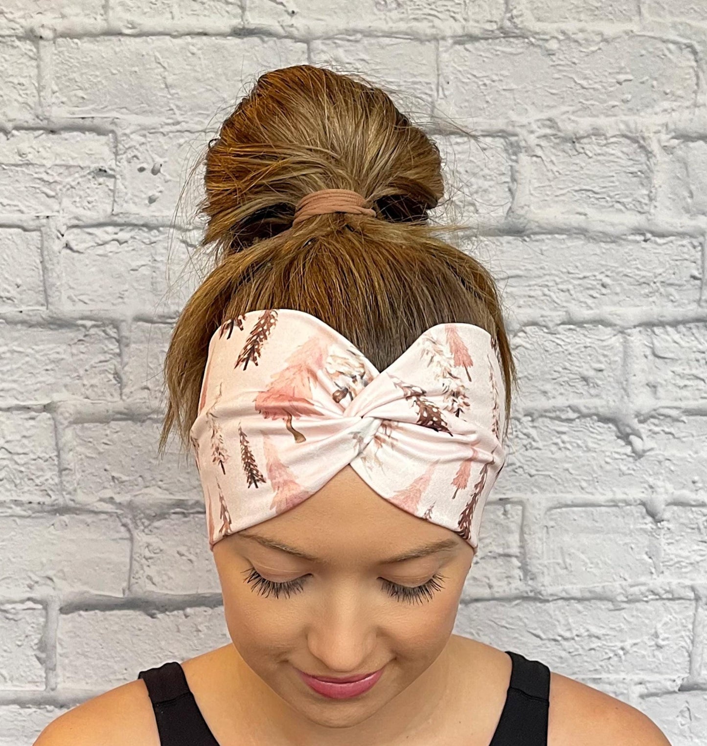 Woman with hair in bun wearing wide, twisted headband in light pink with Christmas tree print.