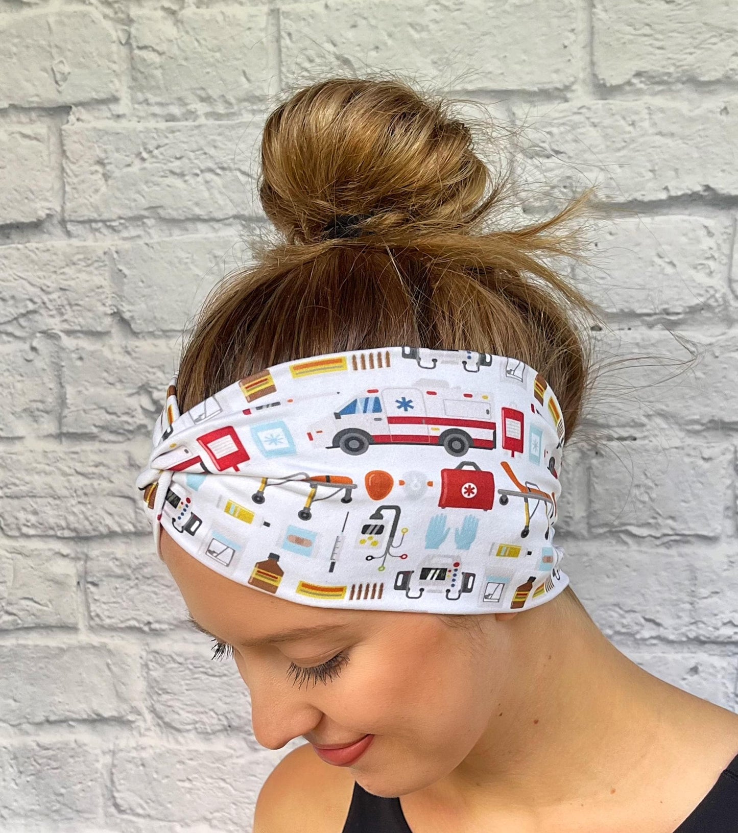 Woman with hair in bun wearing wide, twisted headband in white with ambulance/emergency theme print.