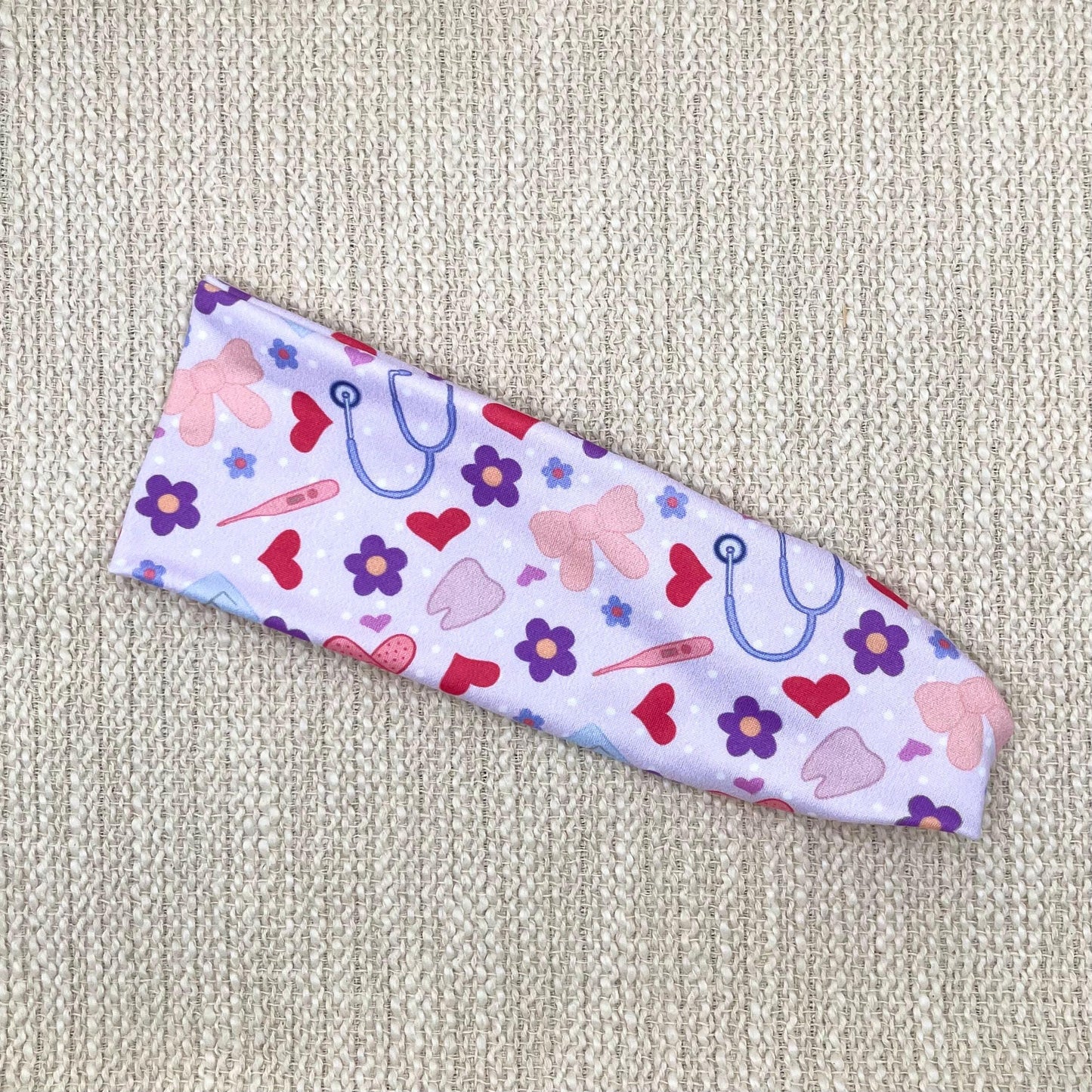 Flat, stretchy, lavender color headband with medical, heart, and flower theme print.