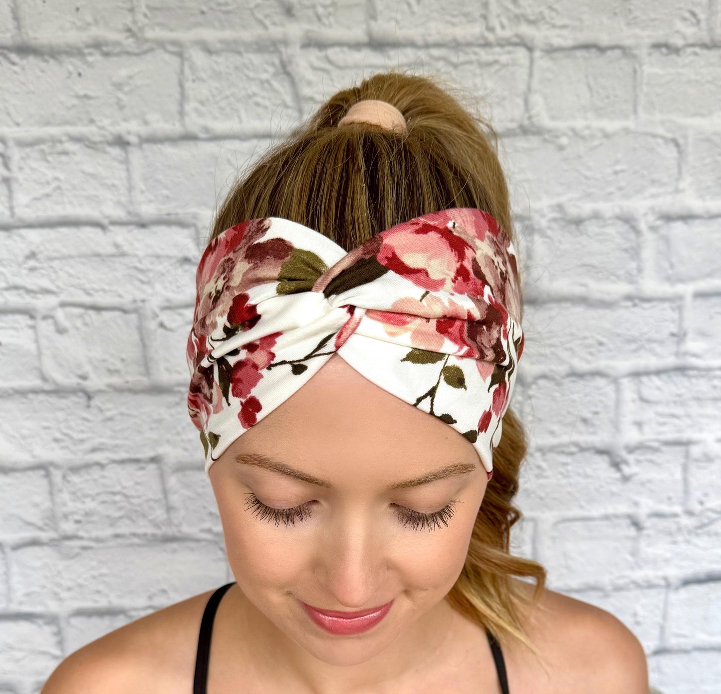 Woman with hair in ponytail wearing wide, twisted headband in white with red/burgundy color floral print.