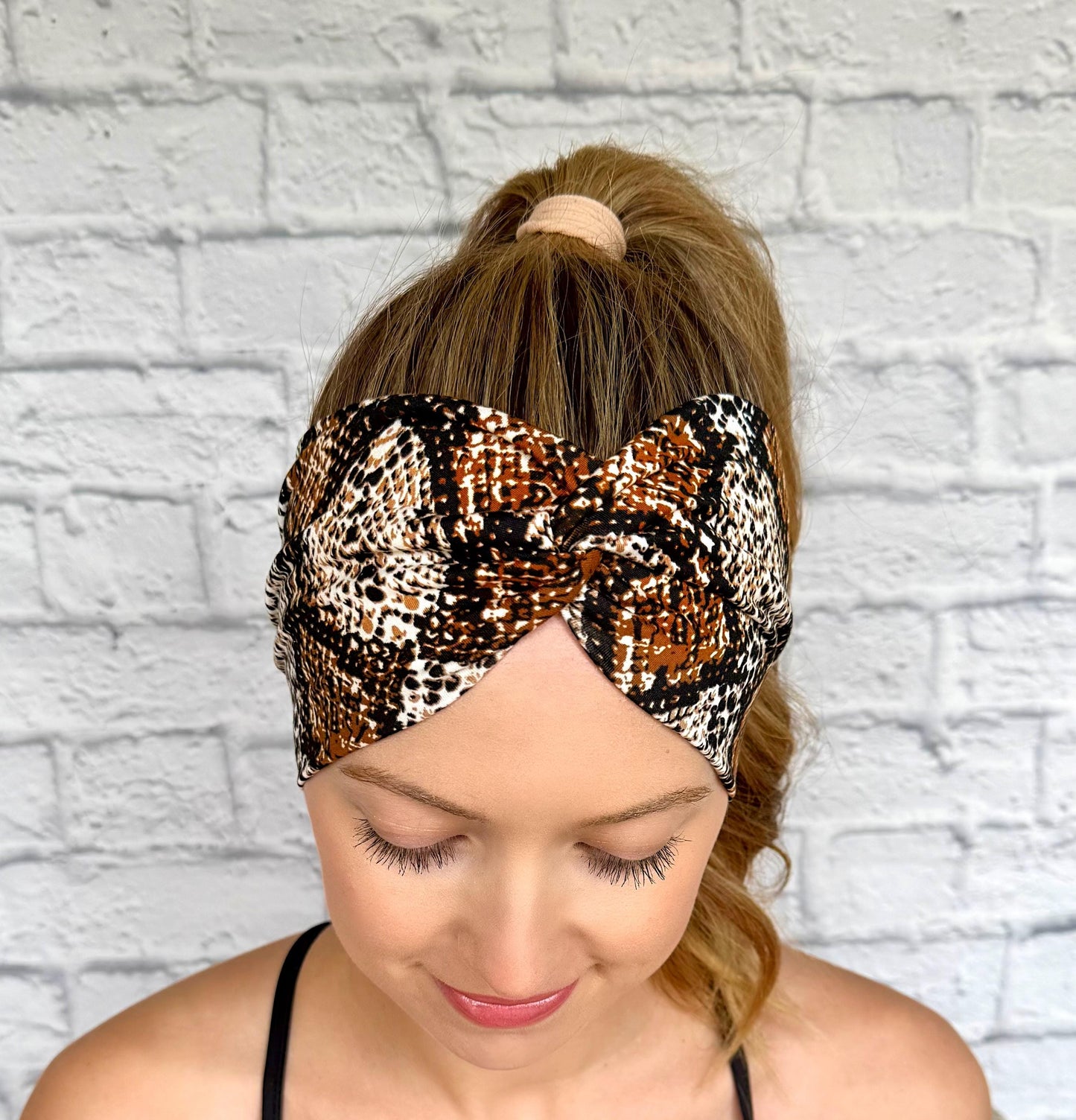 Woman with hair in ponytail wearing wide, twisted headband in brown snakeskin print.