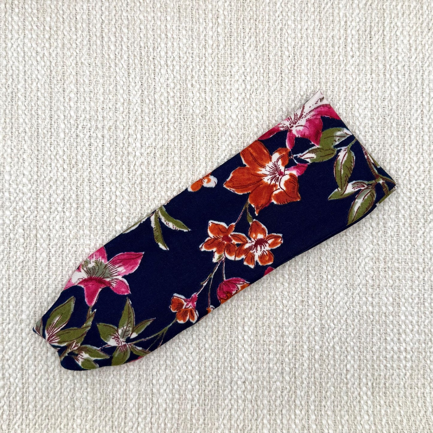 Flat, stretchy, navy color headband with floral print, primarily pink florals.