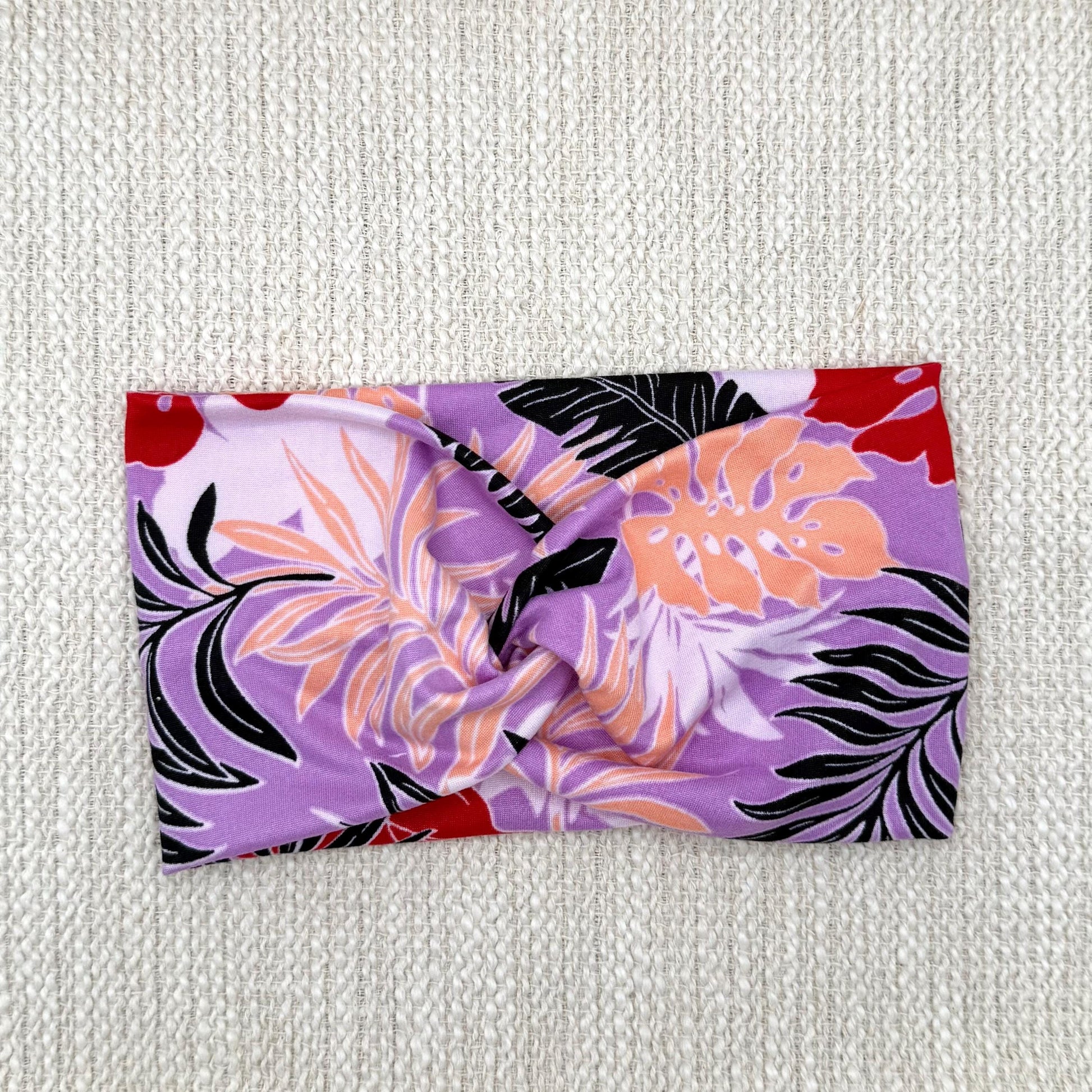 Wide, twisted headband in lavender color with black, peach, white, and red floral print.