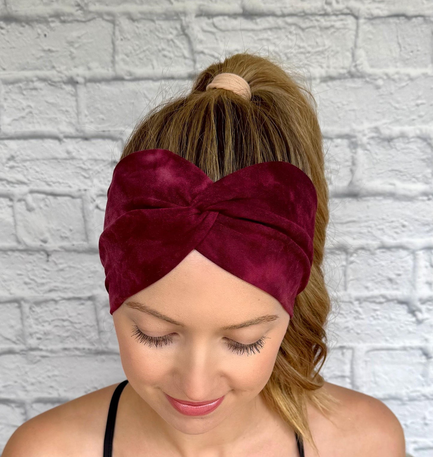 Woman with hair in ponytail wearing wide, twisted headband in maroon tie dye print.