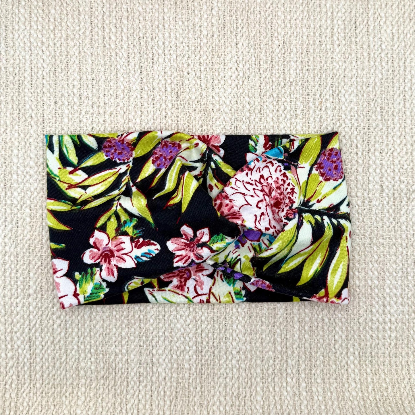 Wide, twisted headband in black with lime green, pink, white, and purple floral print.