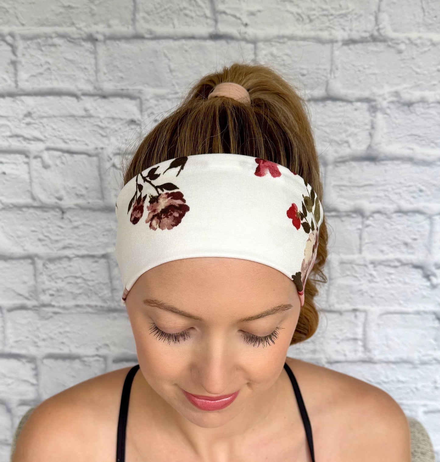 Woman with hair in ponytail wearing flat, stretchy headband in white with maroon rose print.