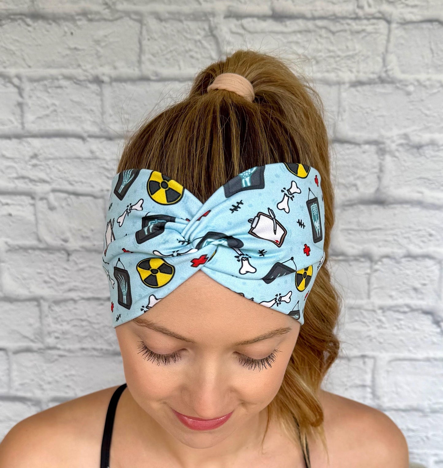 Woman with hair in ponytail wearing wide, twisted, blue headband with radiology theme print.
