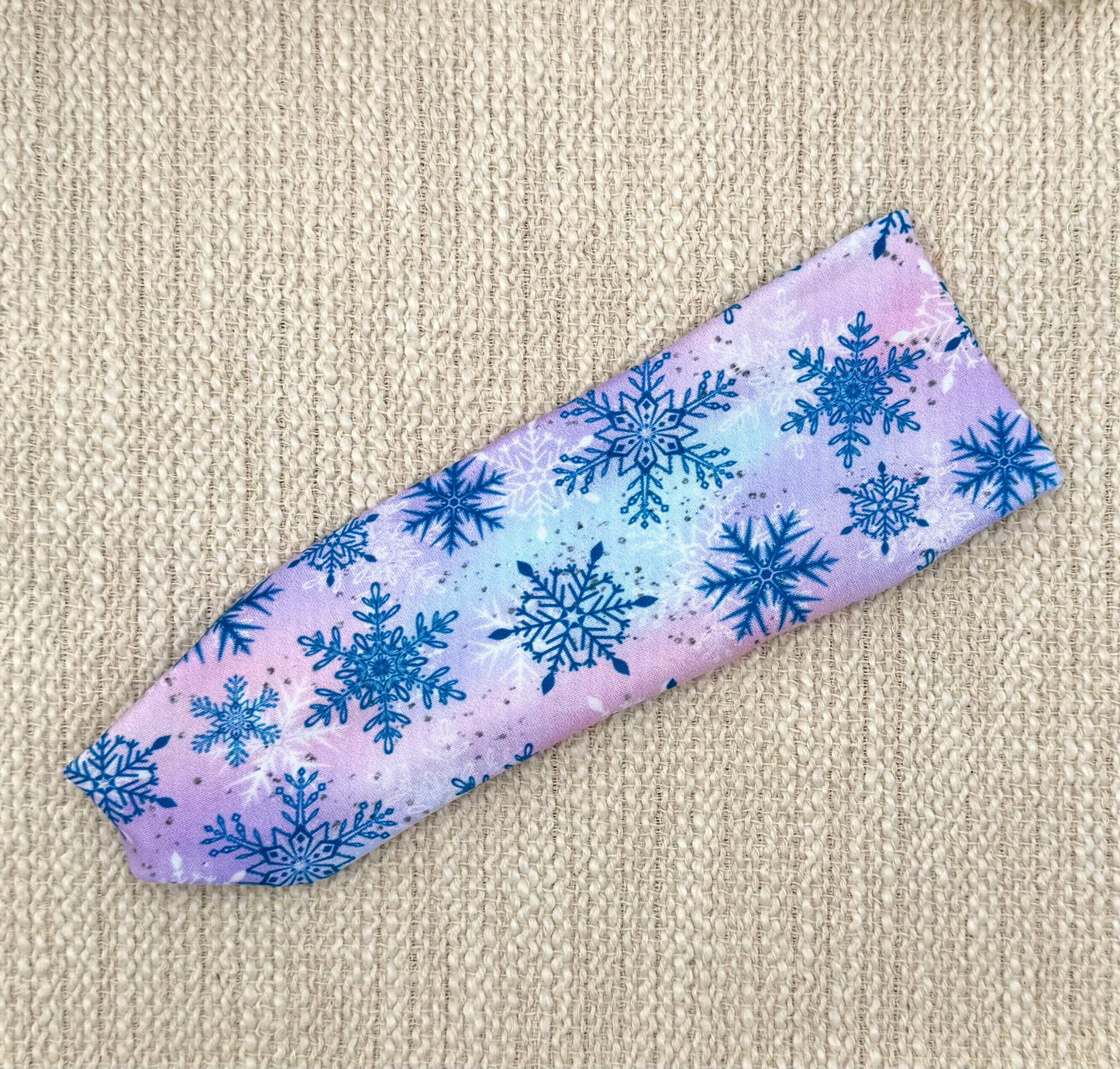 Flat, stretchy headband with pink, purple, and blue tie dye with blue snowflake print.