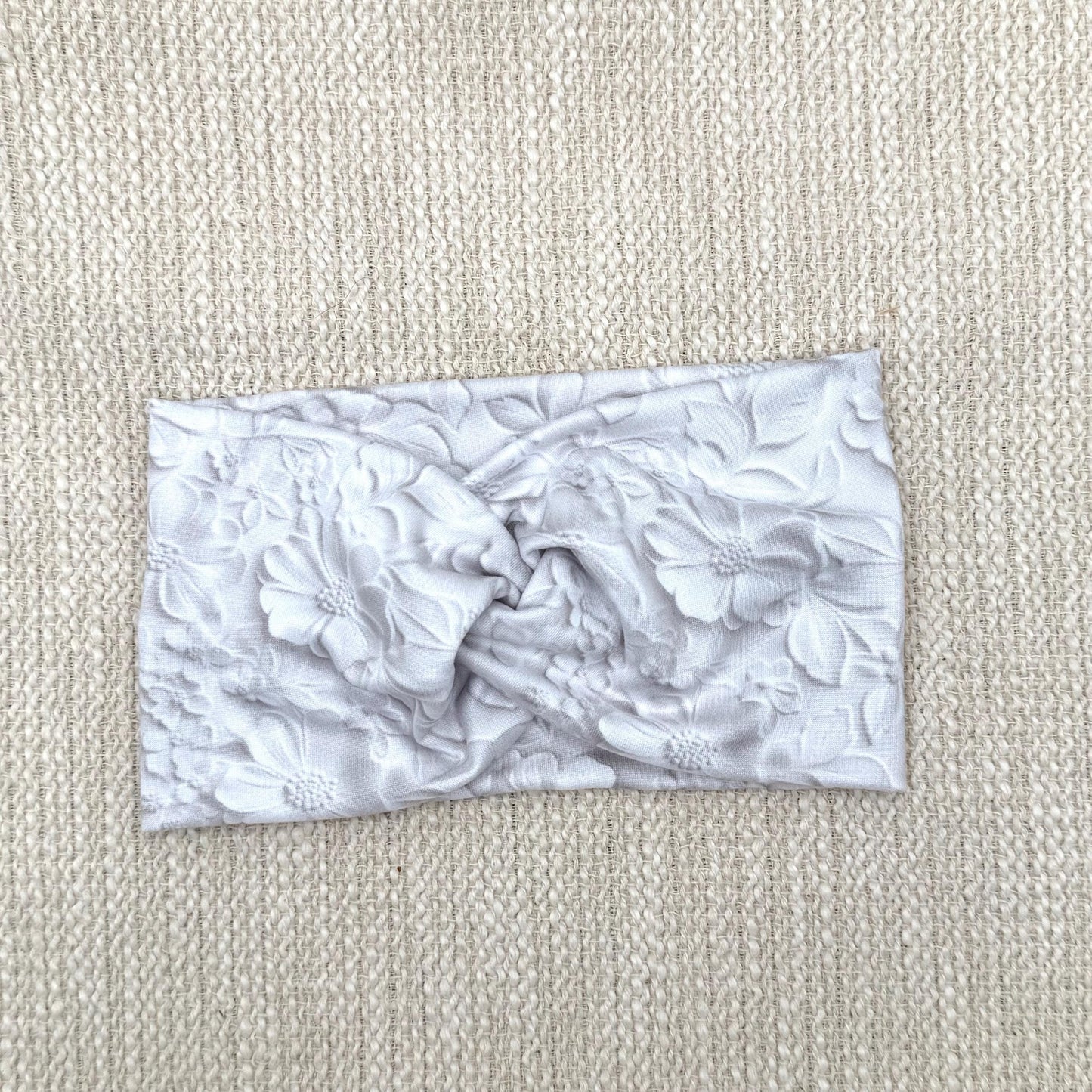 Wide, twisted, white headband with faux embossed floral print and gray shadowing.