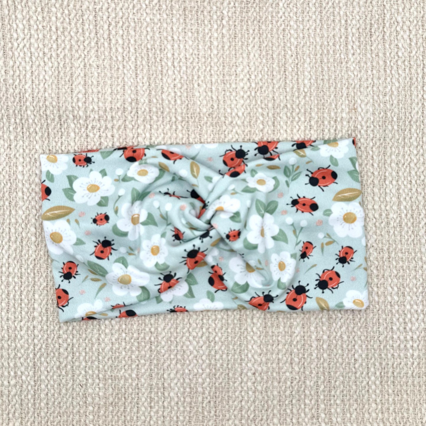 Wide, twisted, light blue headband with ladybug and white floral print.