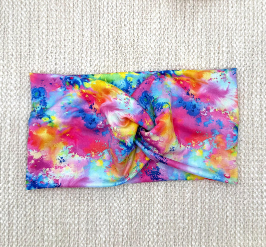 Wide, twisted headband in rainbow color paint-splatter looking print.