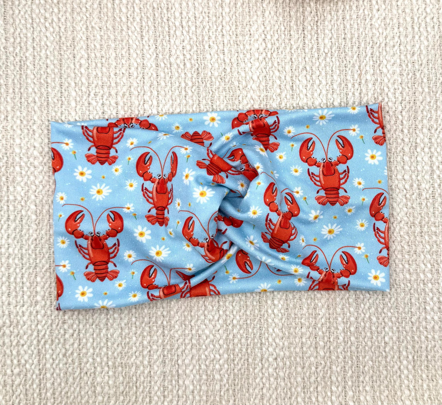 Wide, twisted, light blue headband with lobster and white floral print.