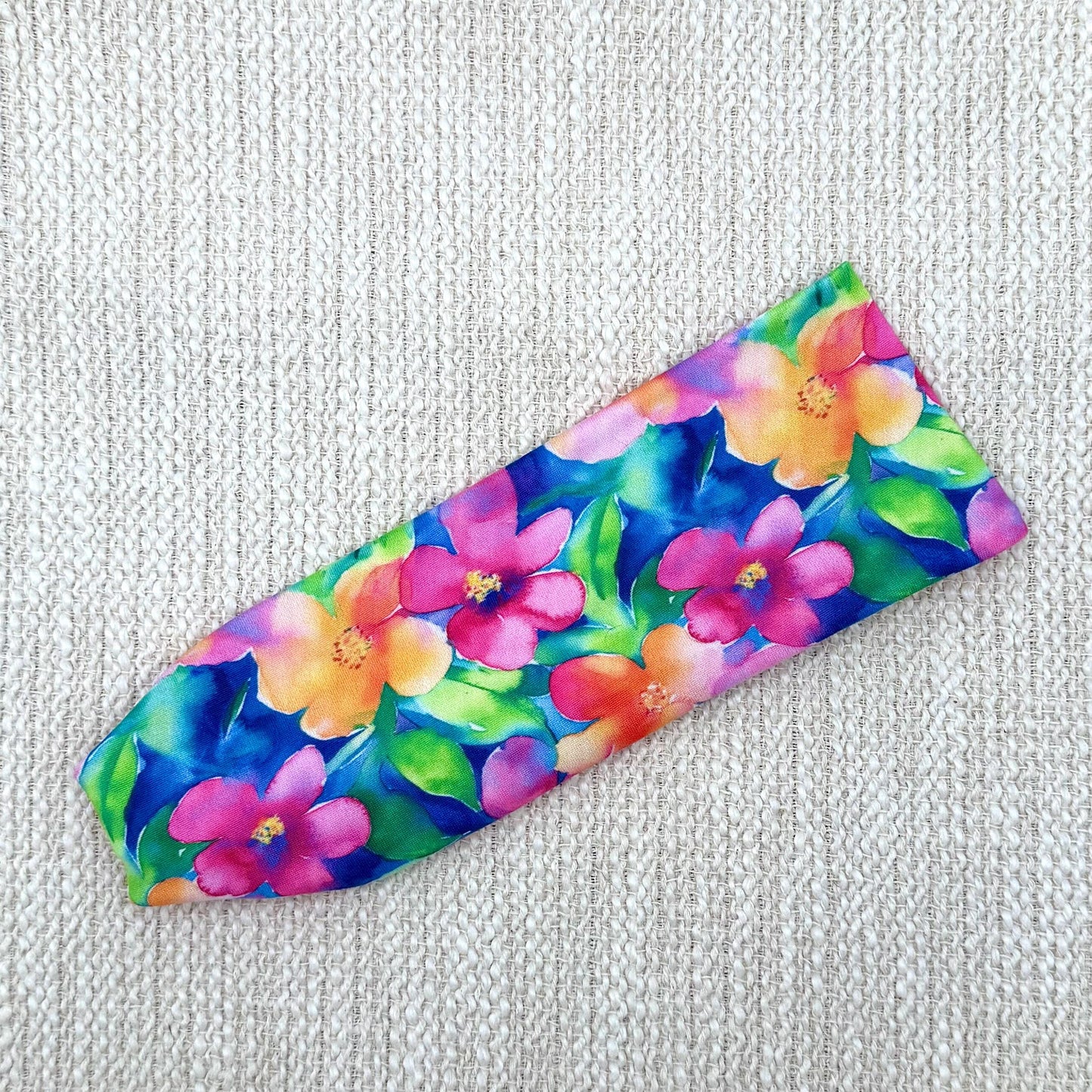 Flat, stretchy headband in blue with bright, multi-color Hawaiian theme floral print.