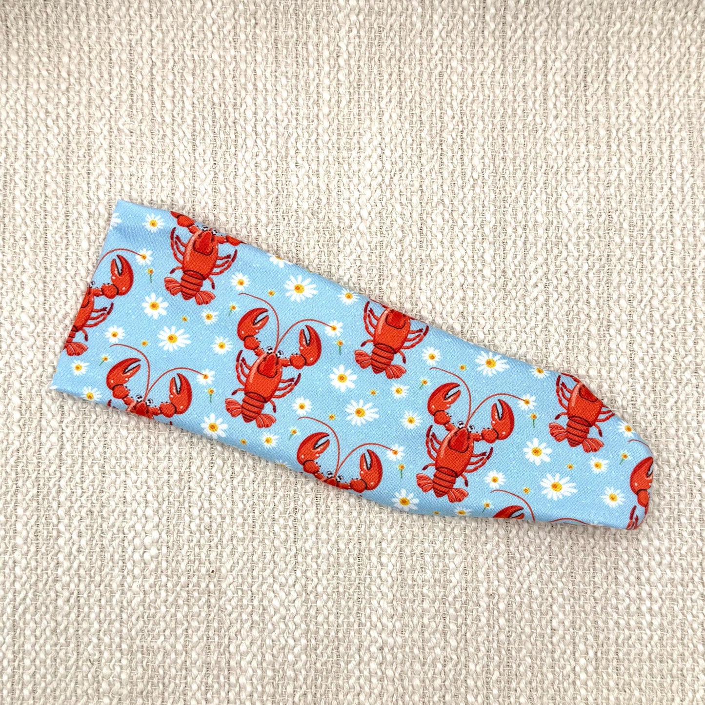 Flat, stretchy headband in light blue with white flower and lobster print.