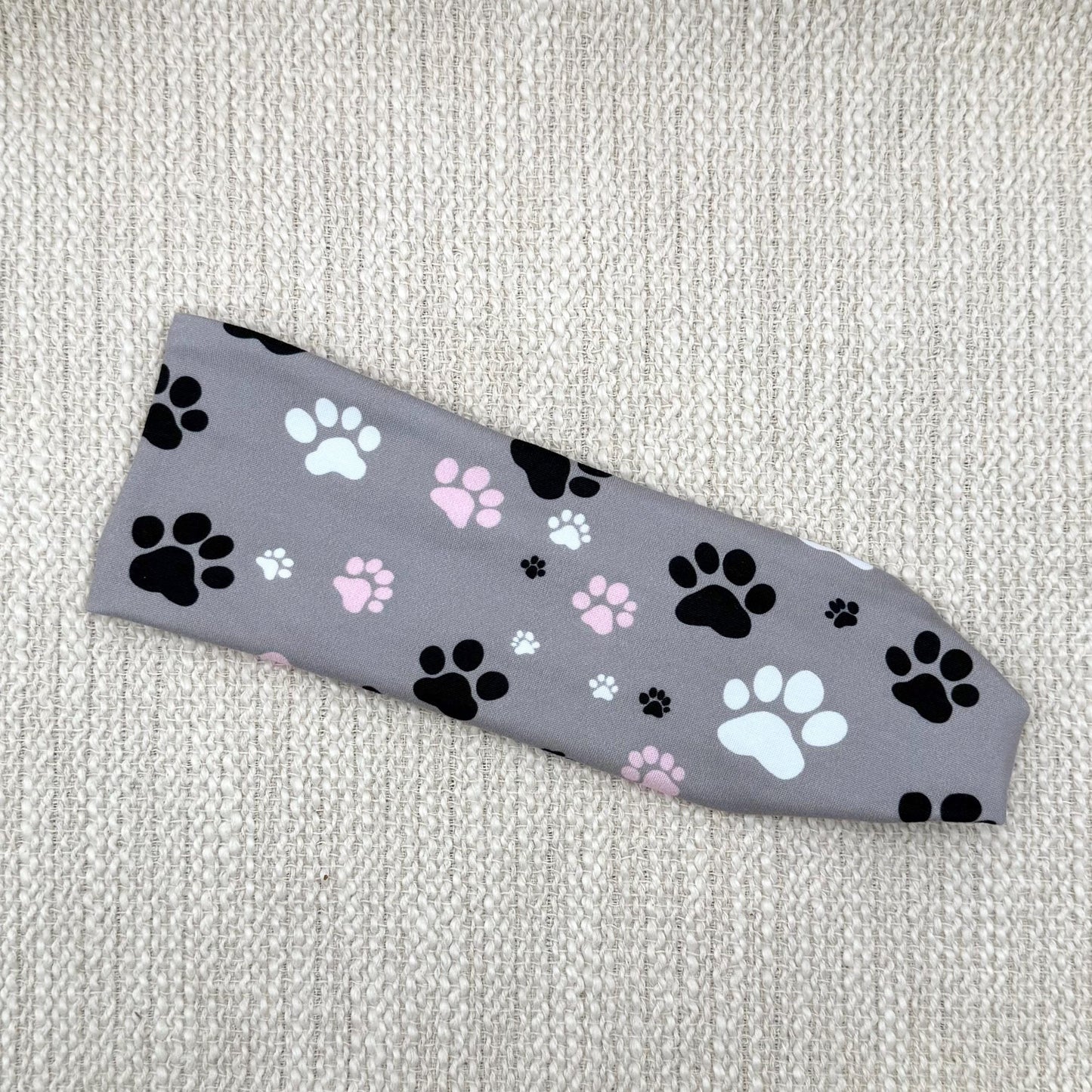 Flat, stretchy headband in gray with white, pink, and black dog paw print.