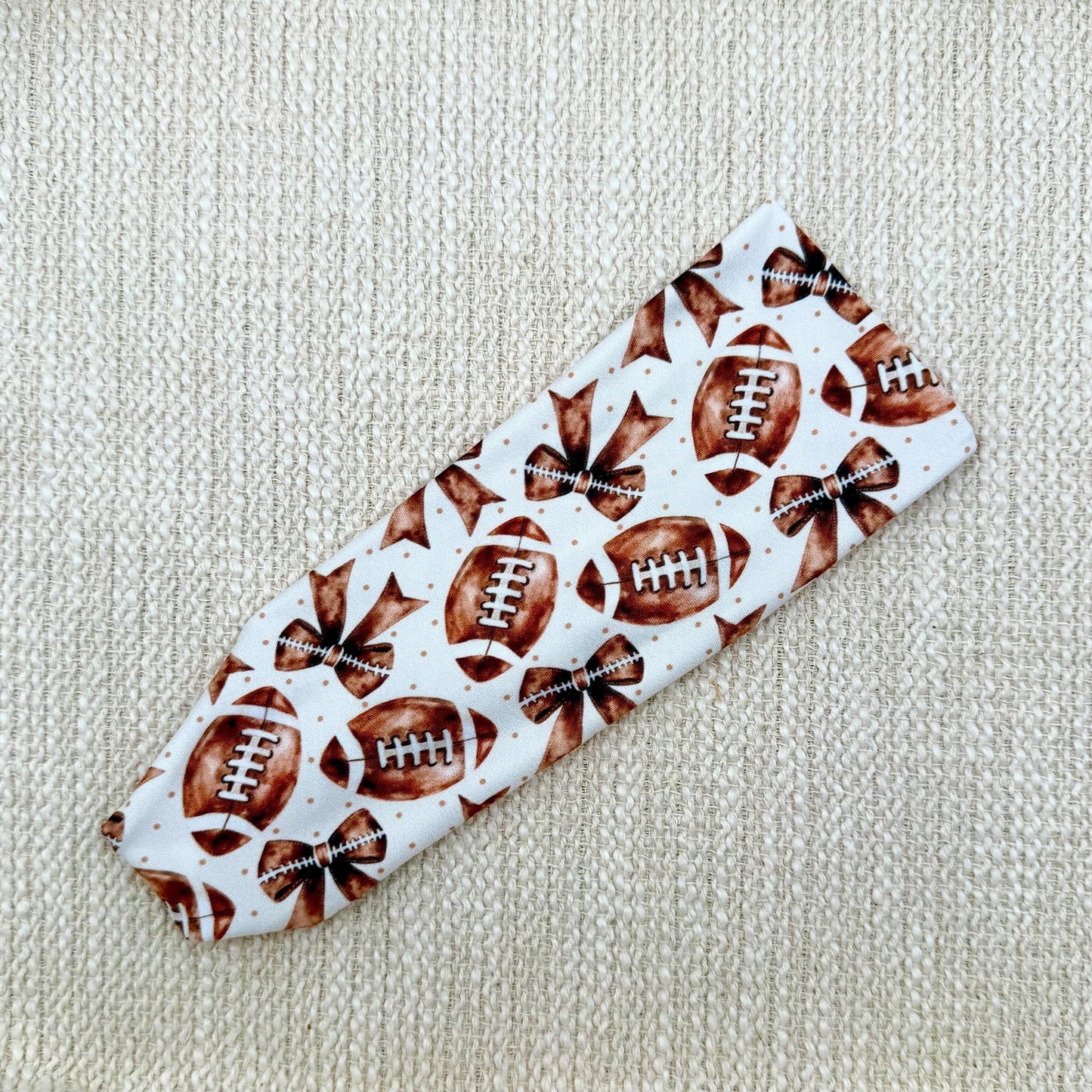 Flat, stretchy headband in white with brown football and bow print.