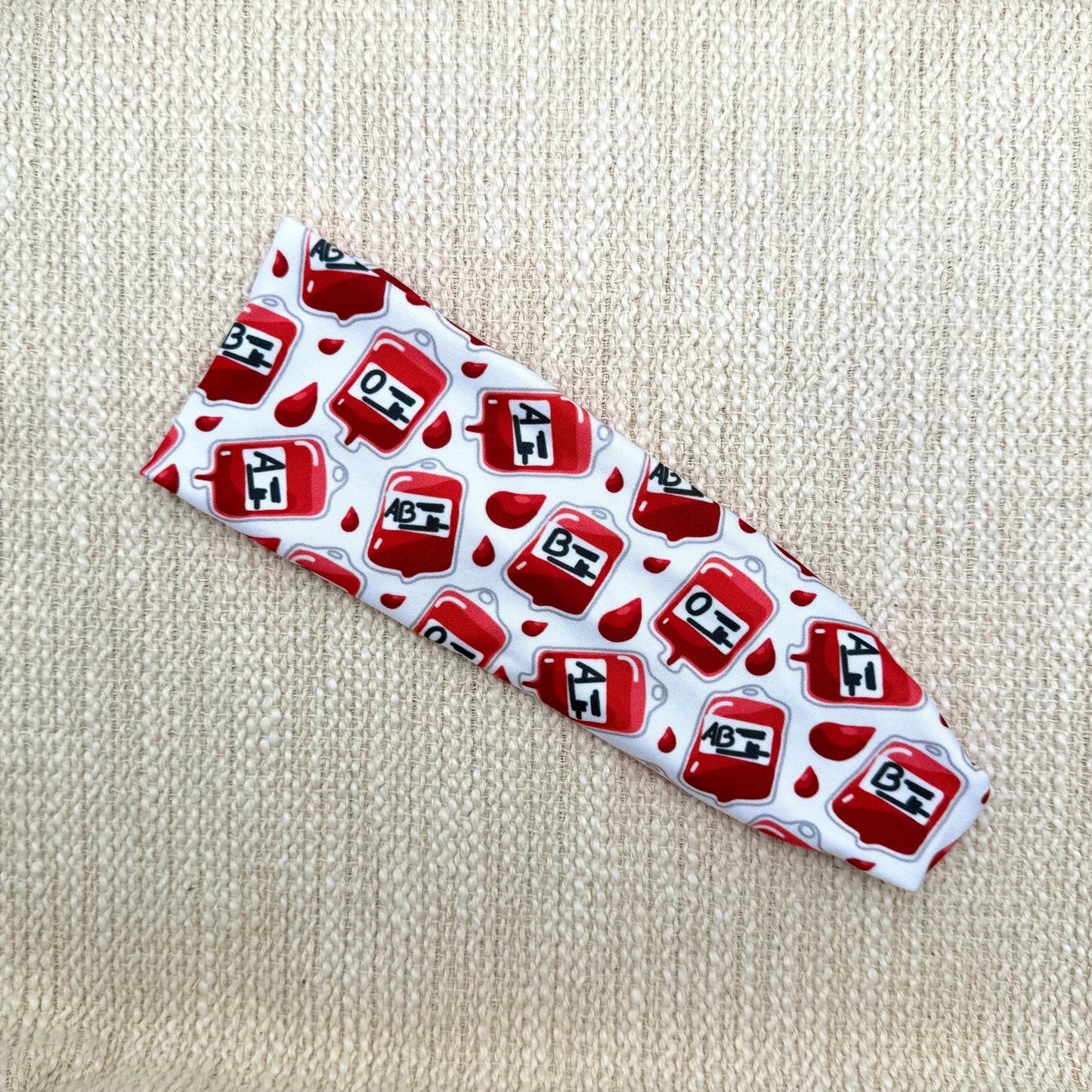 White headband with phlebotomy theme print displayed on a cream background.