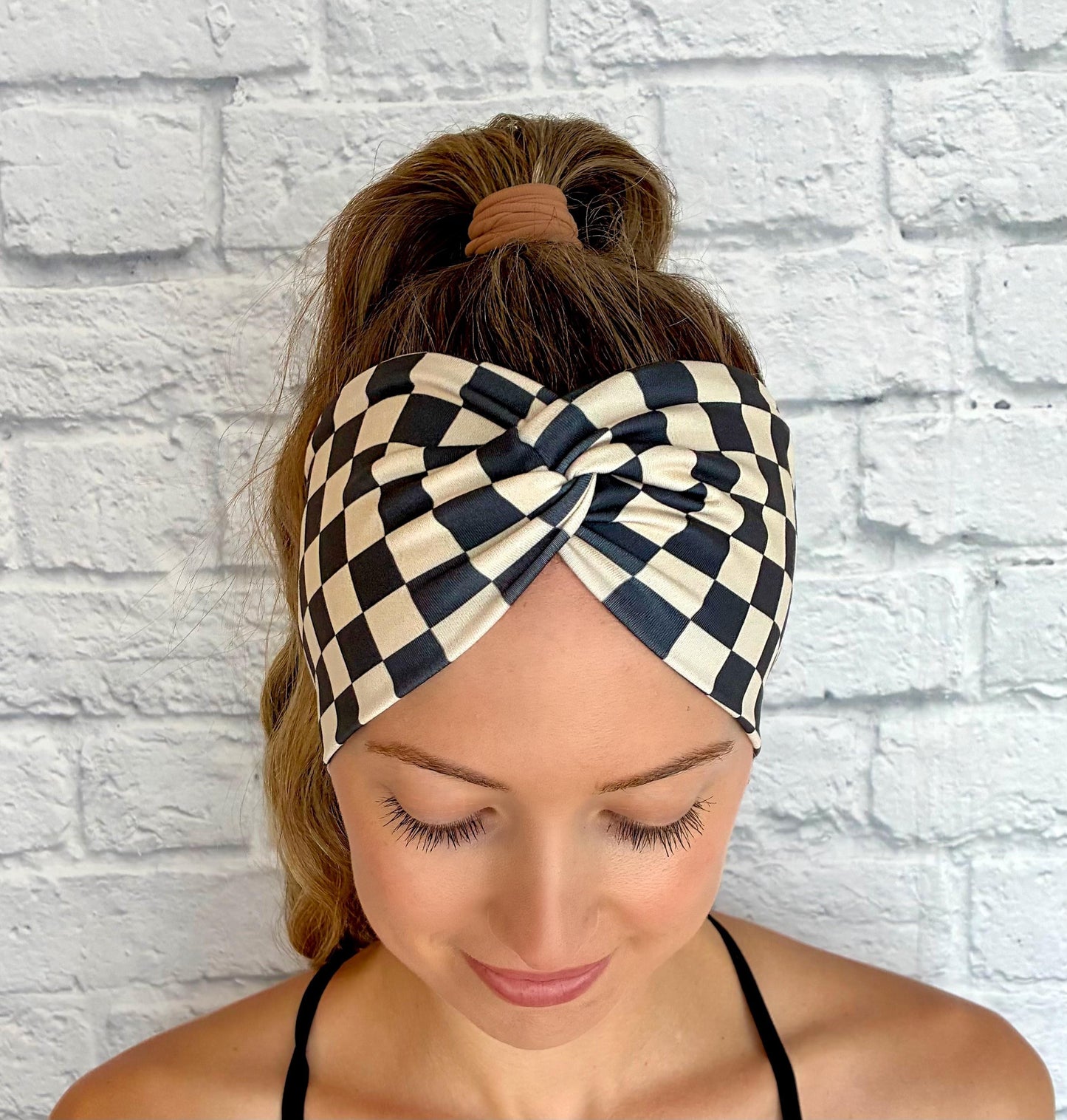 Woman with hair in ponytail wearing wide, stretchy headband in black and tan checker print.