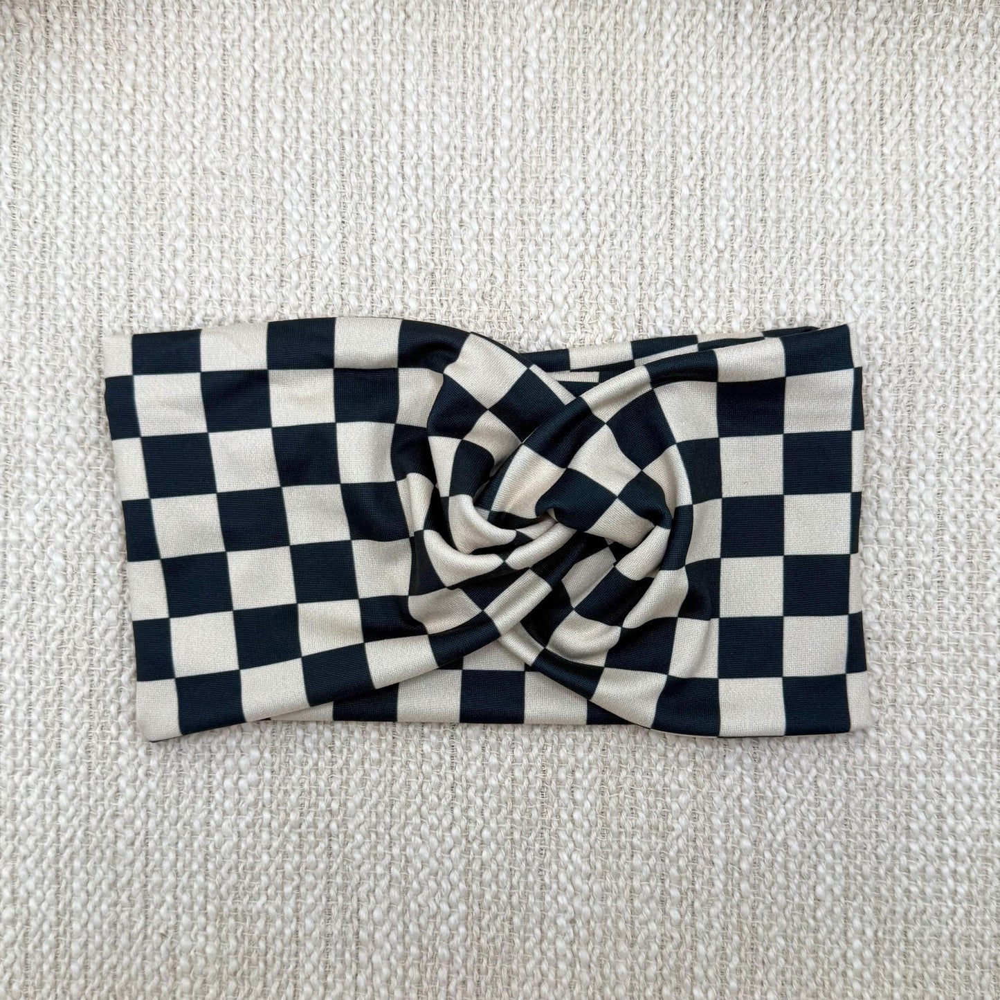 Wide, stretchy headband in black and tan checker print displayed on a cream color background.