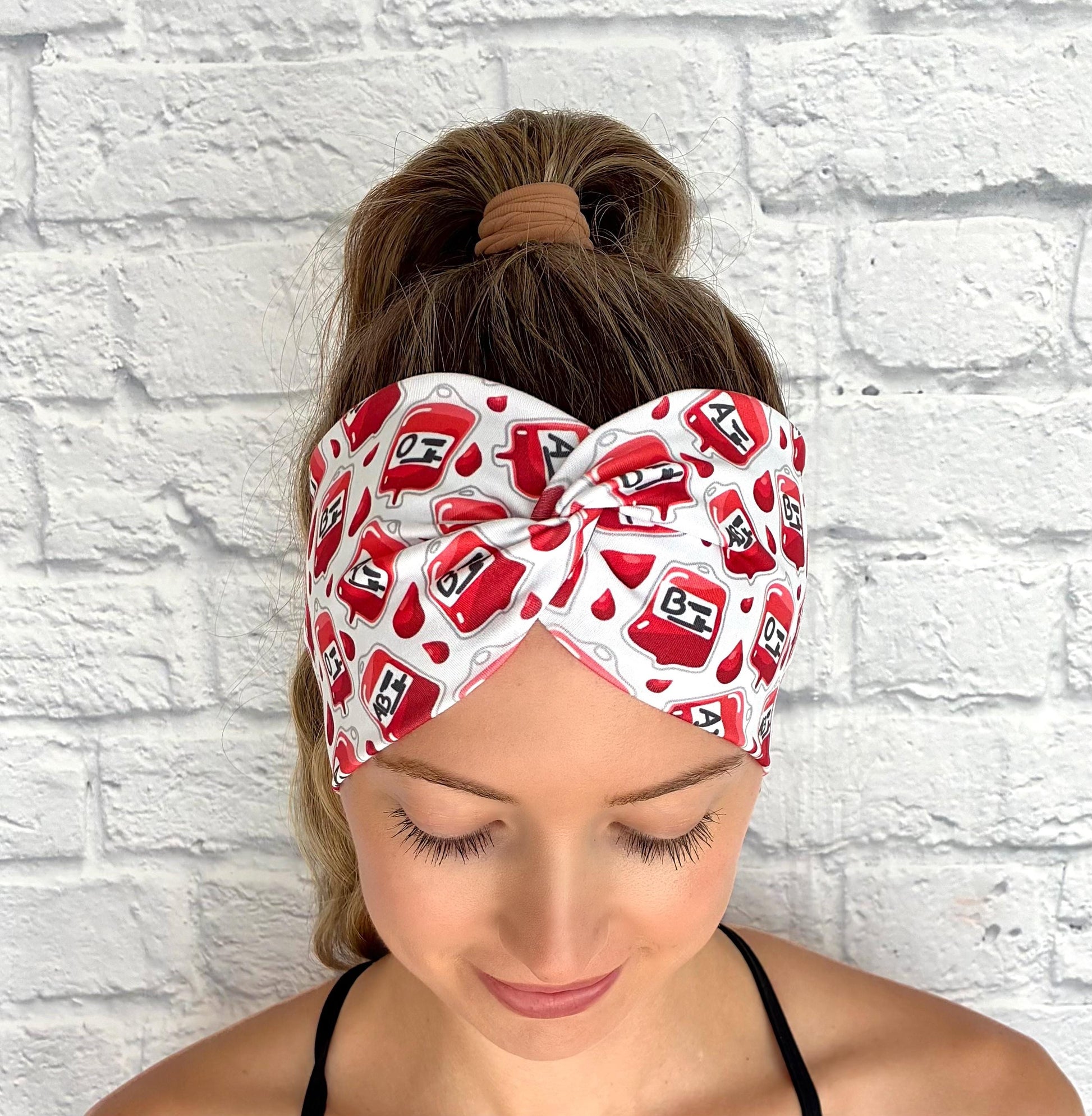 Woman with hair in ponytail wearing wide, twisted headband in white with blood/ phlebotomy theme print.