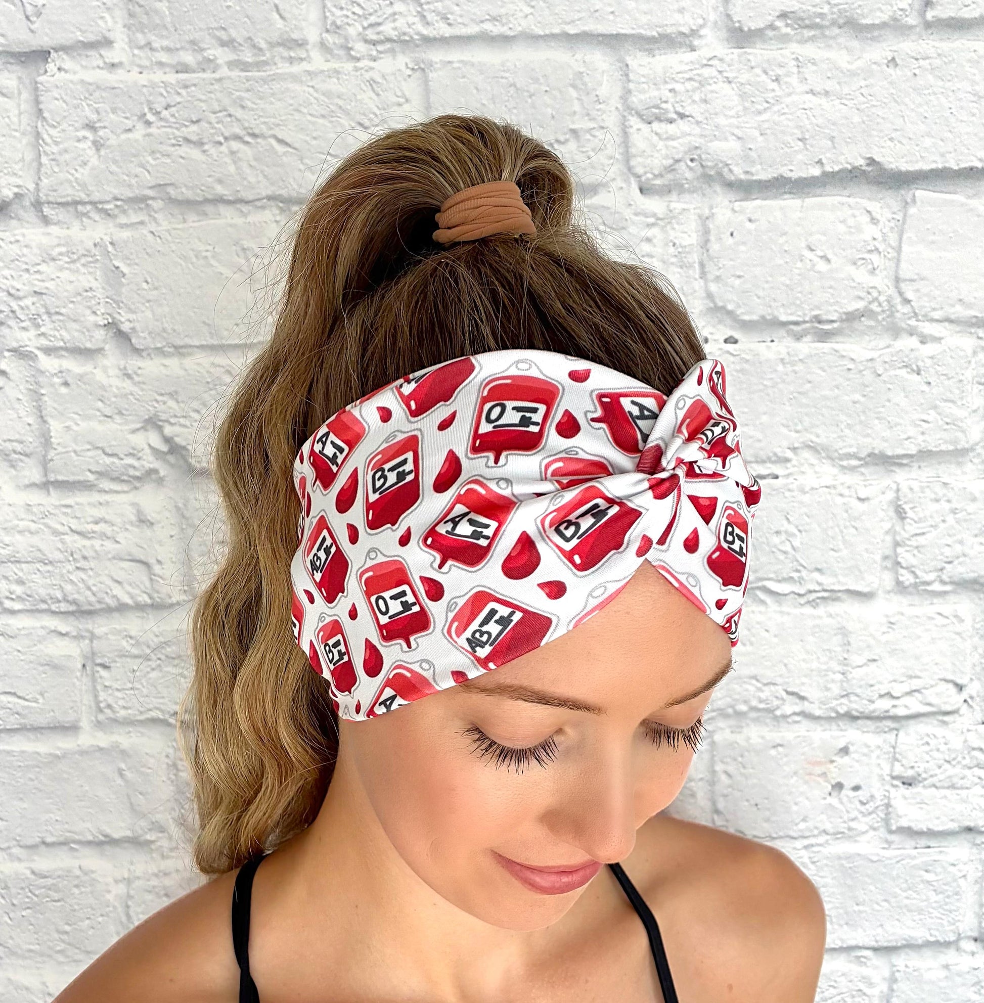 Woman with hair in ponytail wearing wide, twisted headband in white with blood/ phlebotomy theme print.