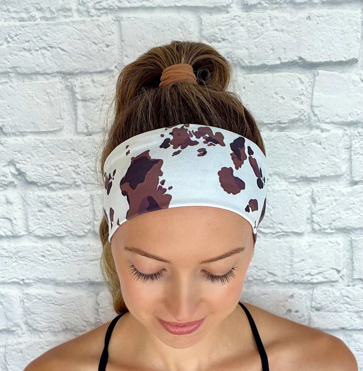 Woman with hair in ponytail wearing flat, stretchy headband in white with cow print.