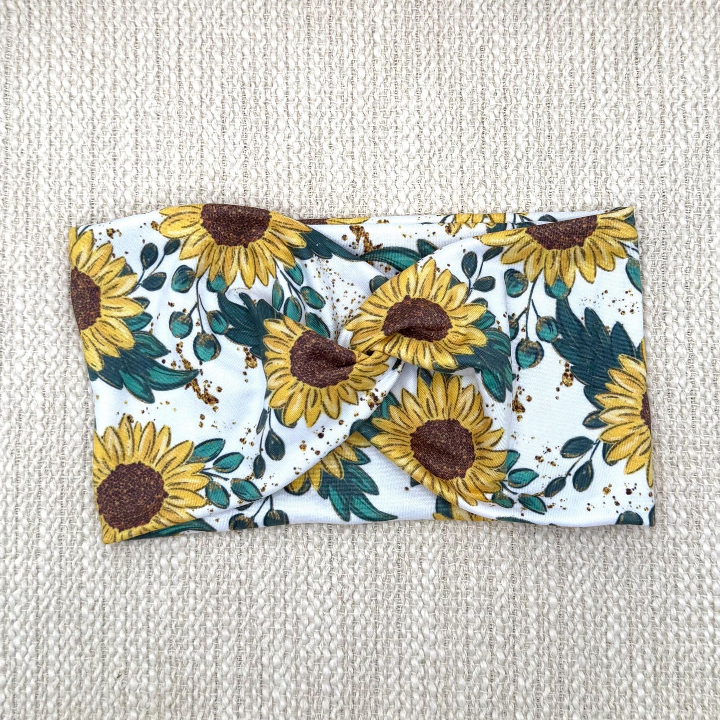 Wide, stretchy headband in white with yellow sunflower print displayed on a cream color background.