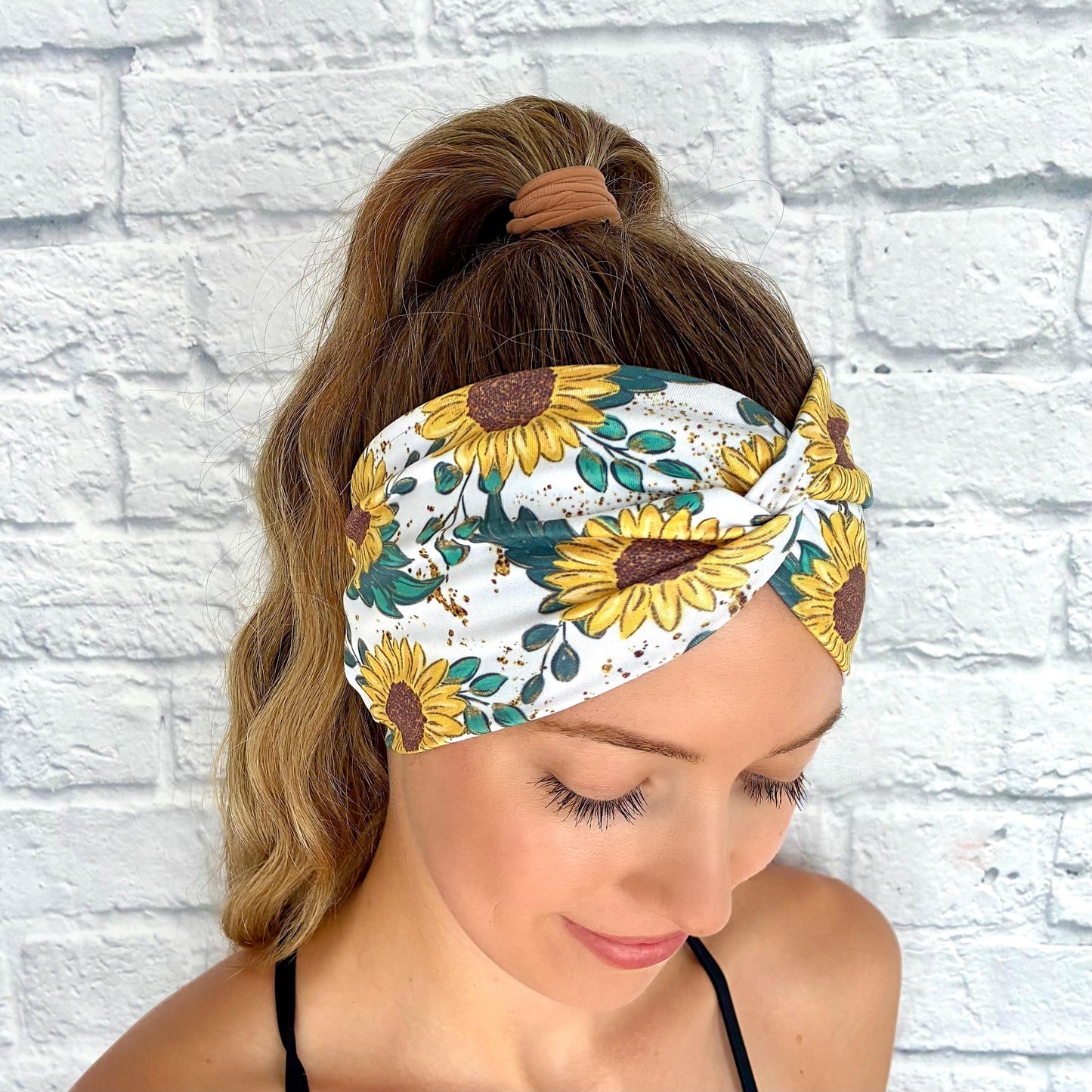 Woman with hair in ponytail wearing white, stretchy headband in white with yellow sunflower print.