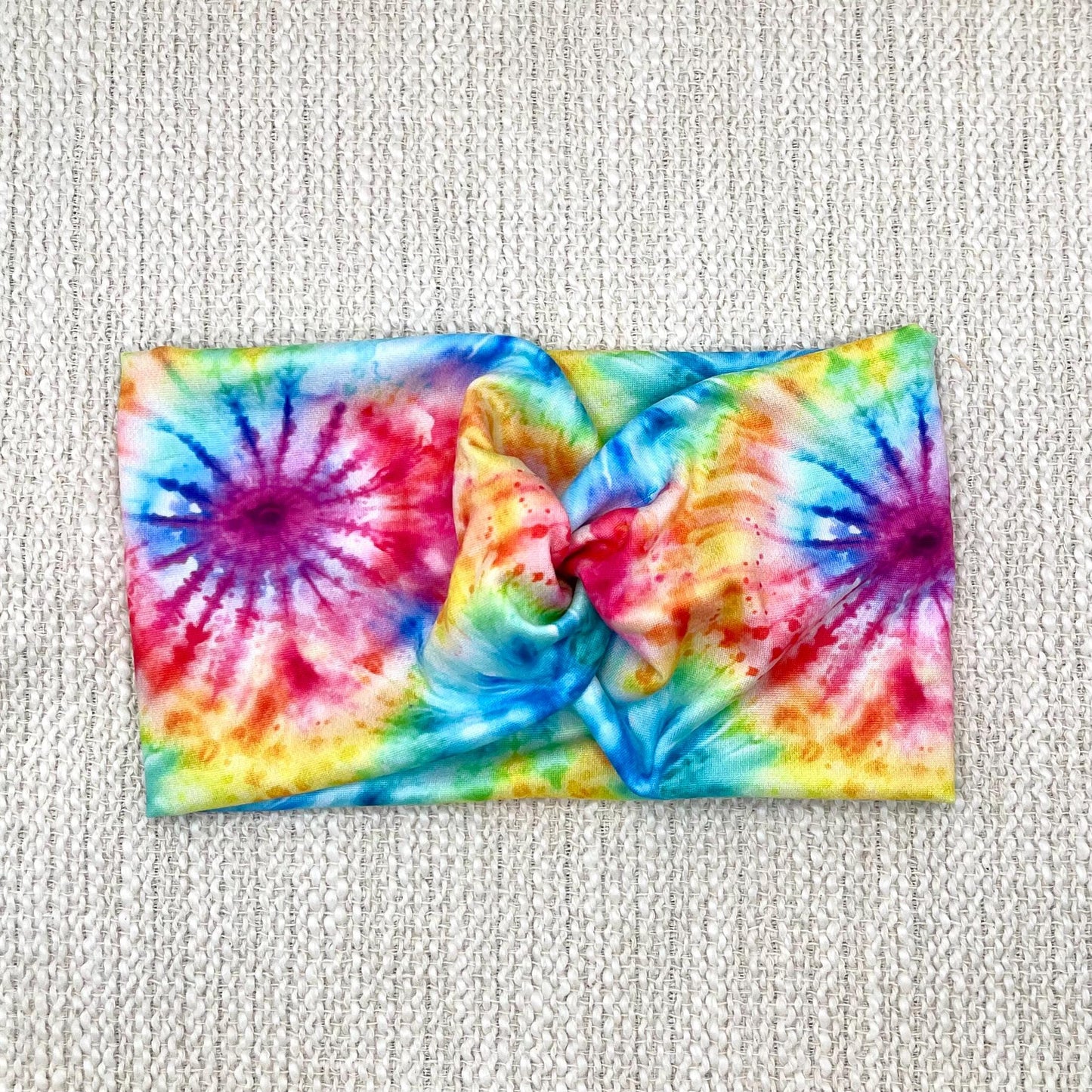 Wide, twisted headband with rainbow color tie dye print.