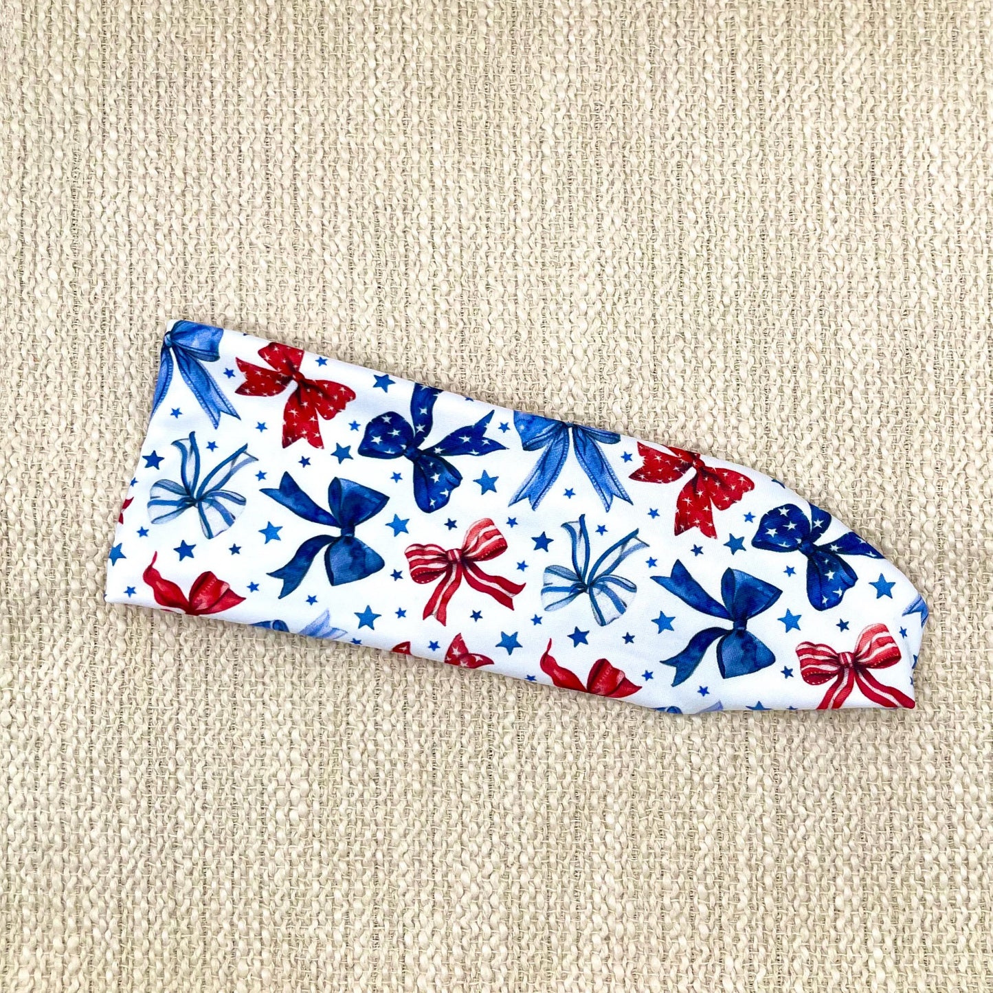 Flat, stretchy, white headband with red and blue bow print and blue stars.